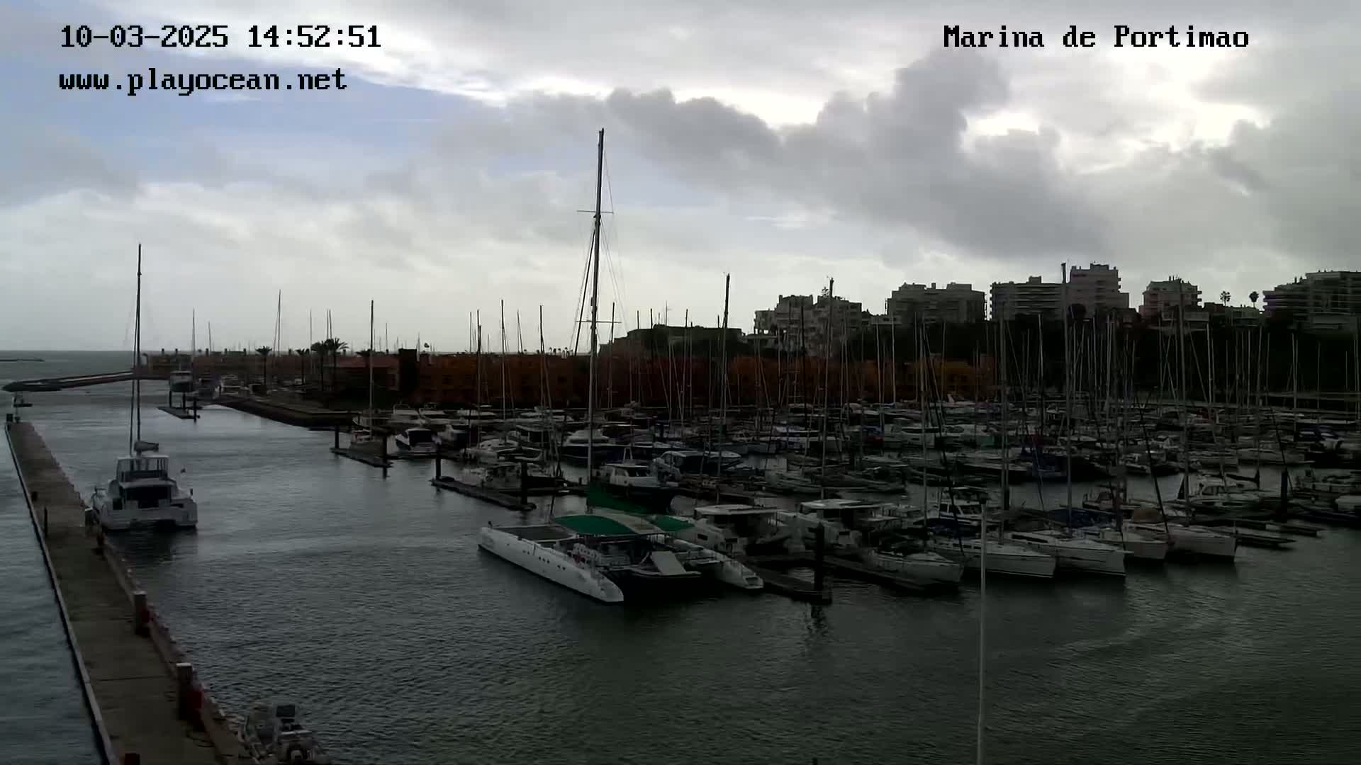 A marina filled with numerous sailboats and motorboats under a cloudy sky.