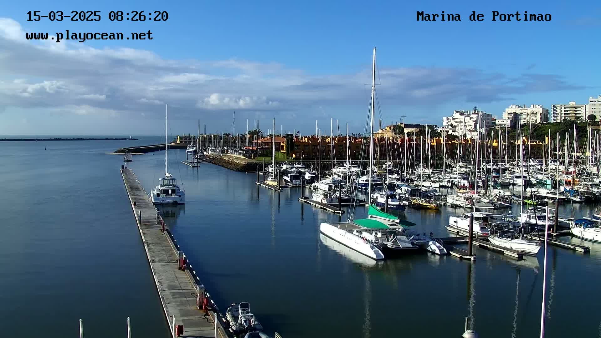 A marina filled with numerous sailboats and motorboats on a partly cloudy day.