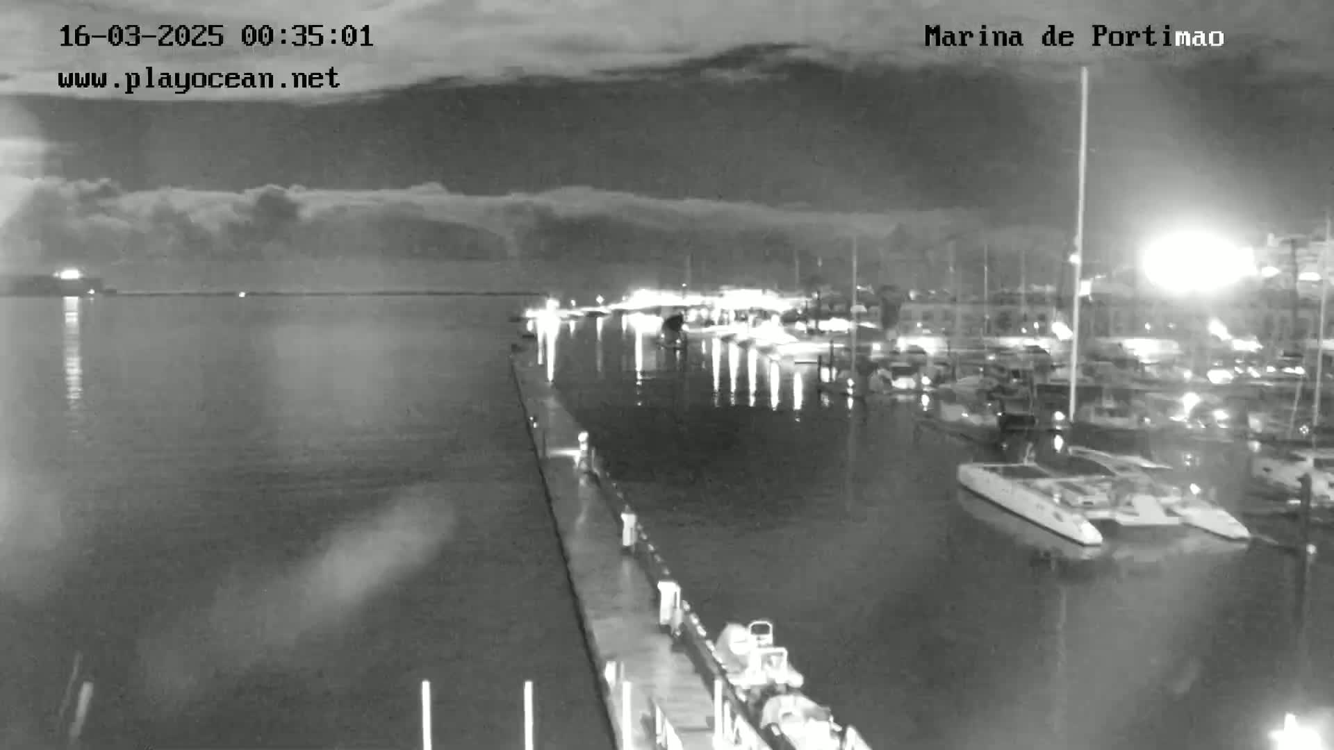 A nighttime, overcast view of a marina filled with boats, seen from a pier.