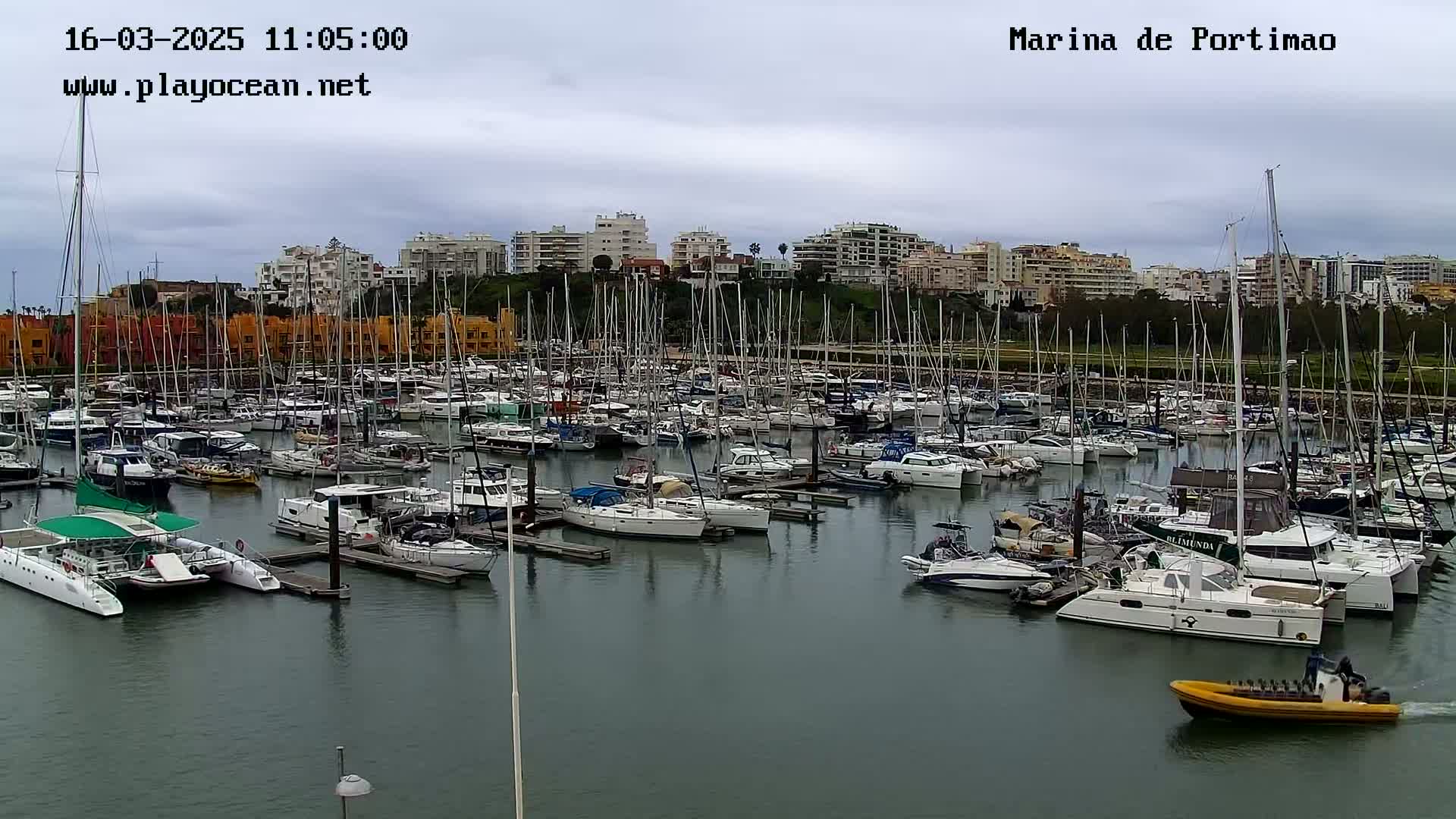 A marina filled with numerous sailboats and motorboats is situated under an overcast sky.