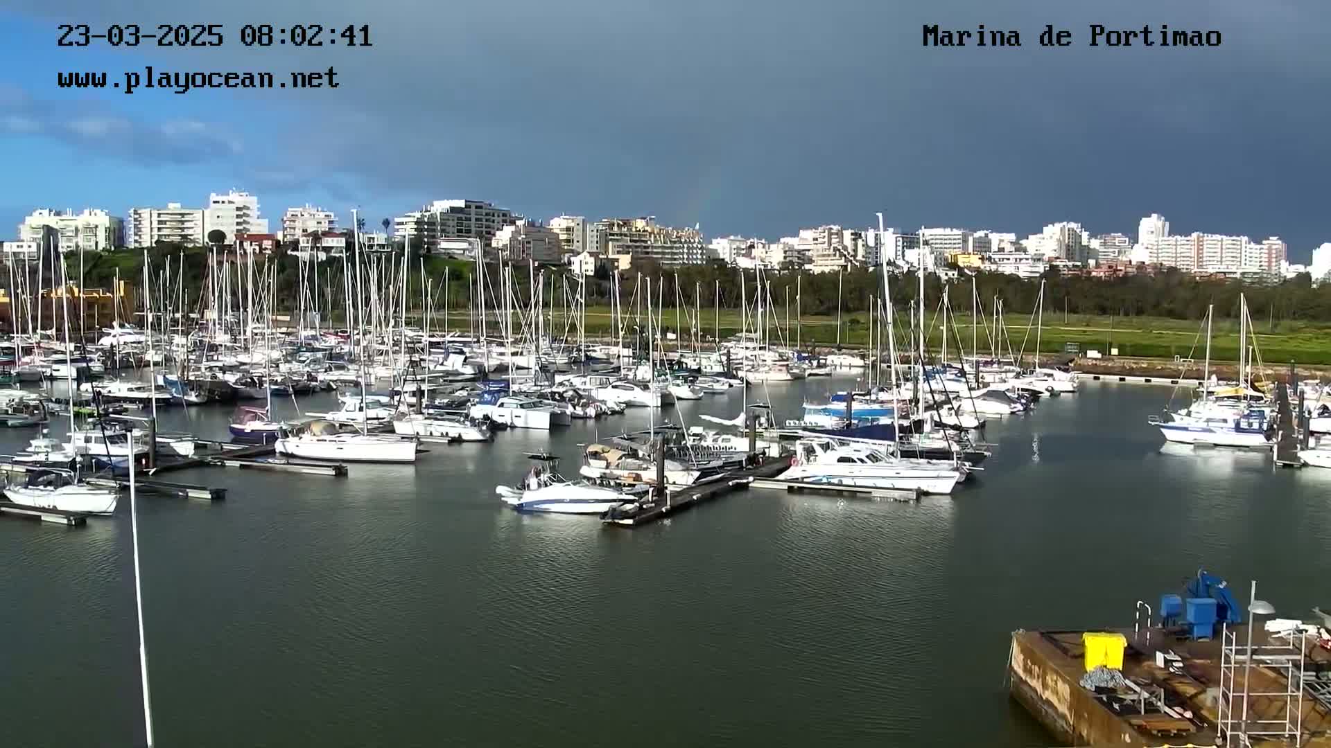Many sailboats are docked in a marina under a partly cloudy sky.