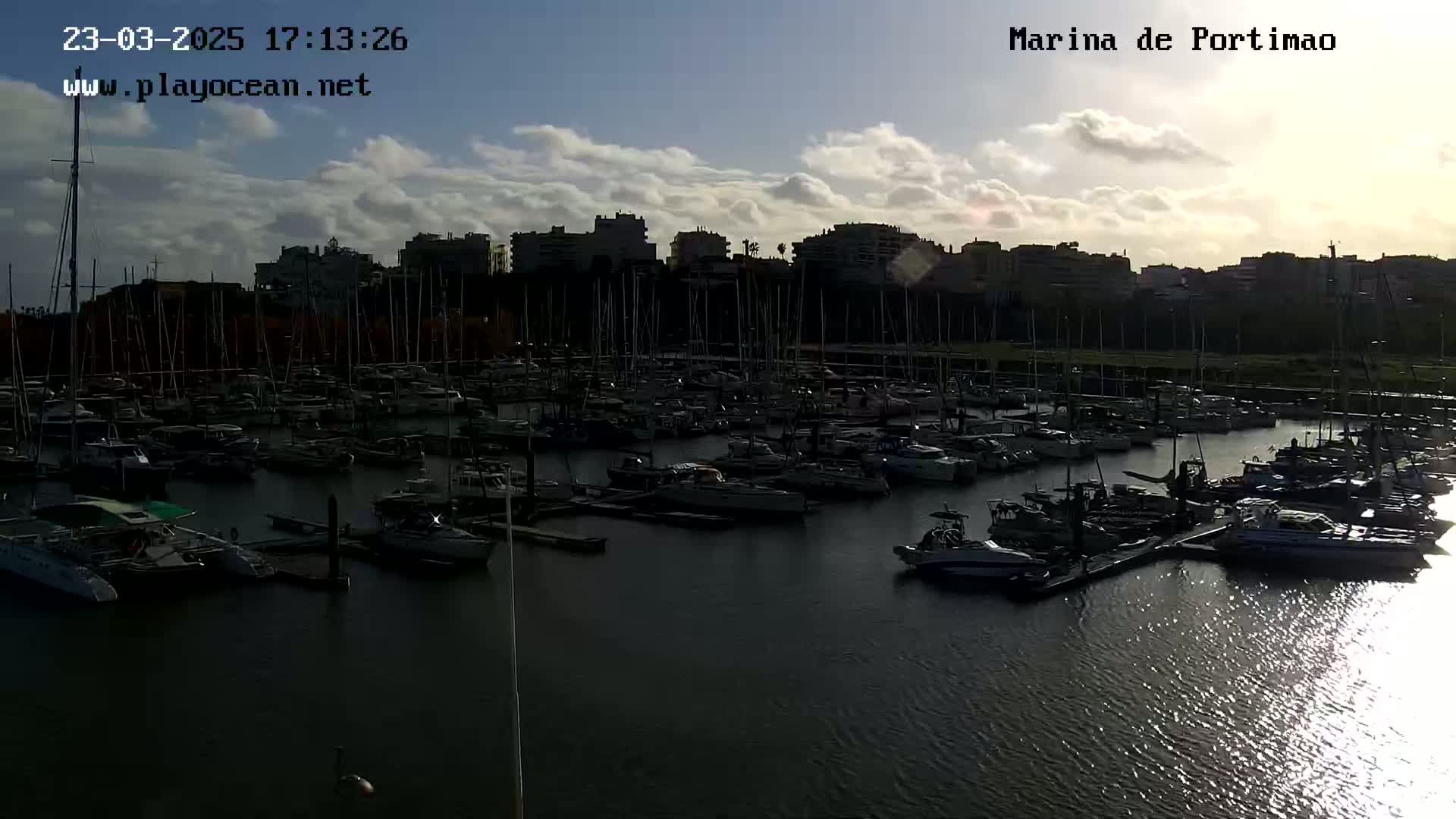 A marina filled with many boats is seen under a partly cloudy sky at sunset.