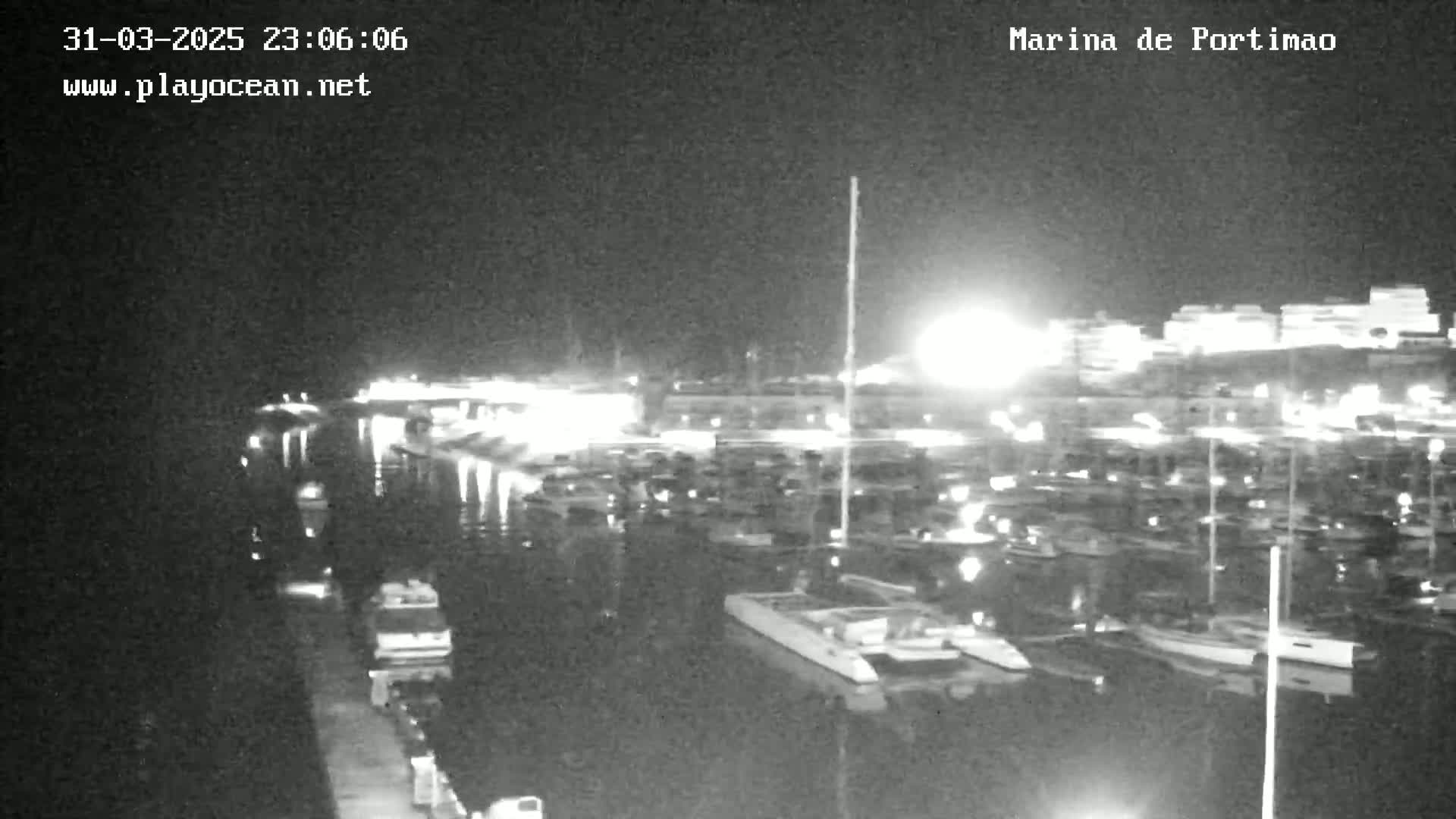 A nighttime view of a marina filled with boats, docked along a calm body of water under a clear, dark sky.
