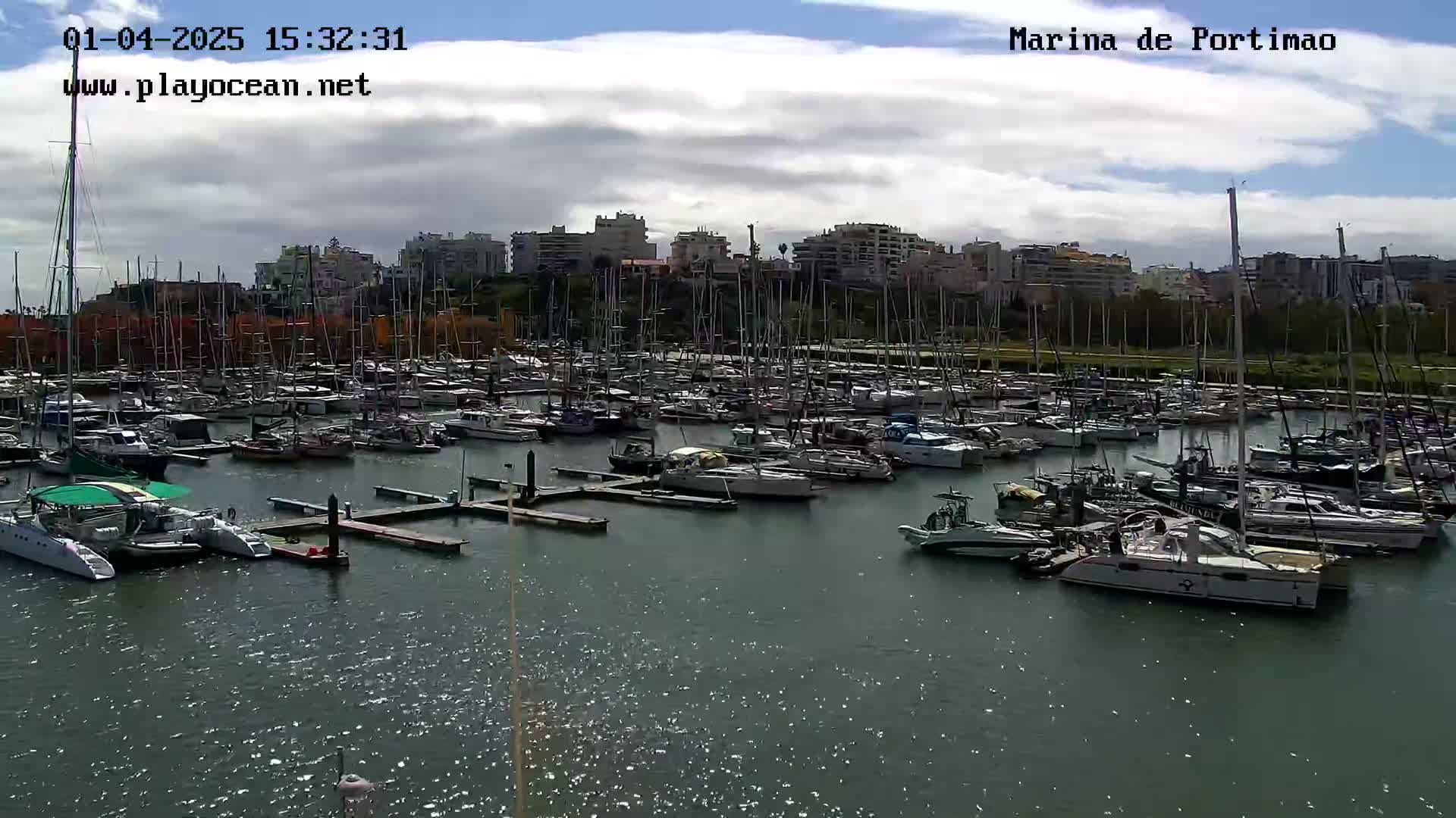Many sailboats and motorboats are docked in a marina under a partly cloudy sky.