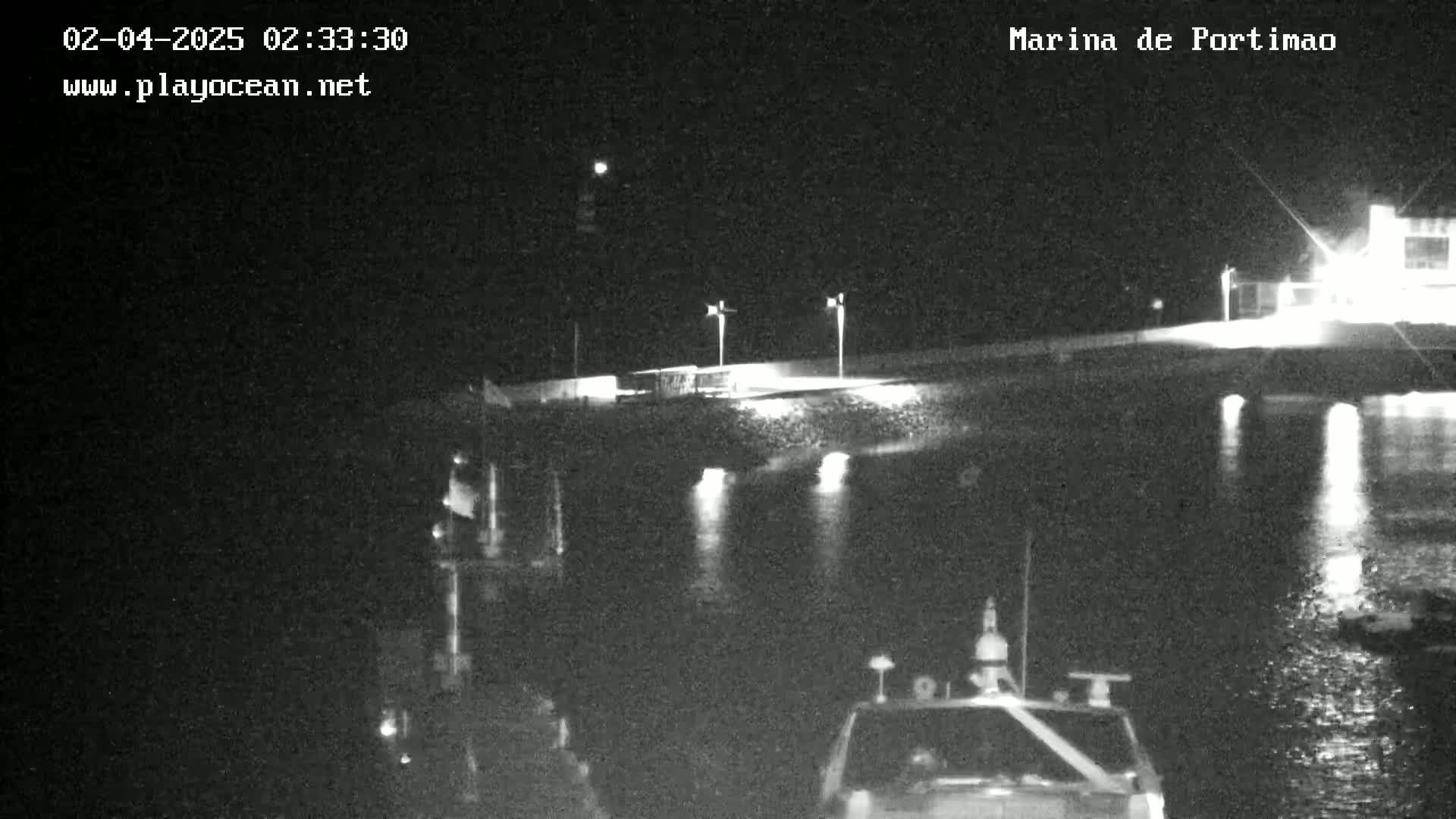 A nighttime, low-light view of a marina with boats on the water and lights illuminating the docks.