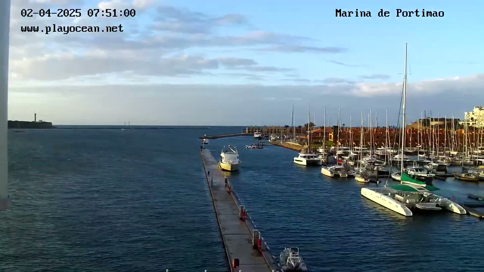 A marina filled with sailboats and motorboats is seen from a pier on a partly cloudy day.