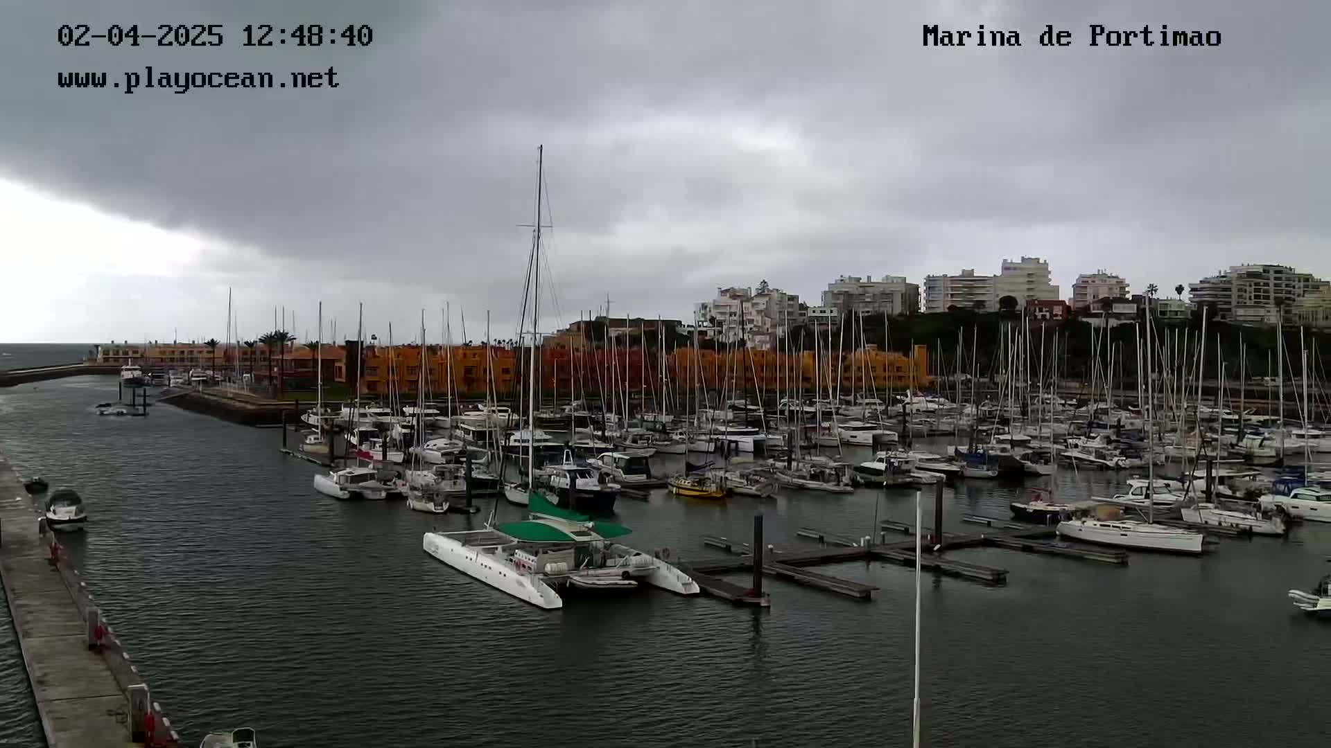 A marina filled with numerous sailboats and motorboats is shown under an overcast sky.
