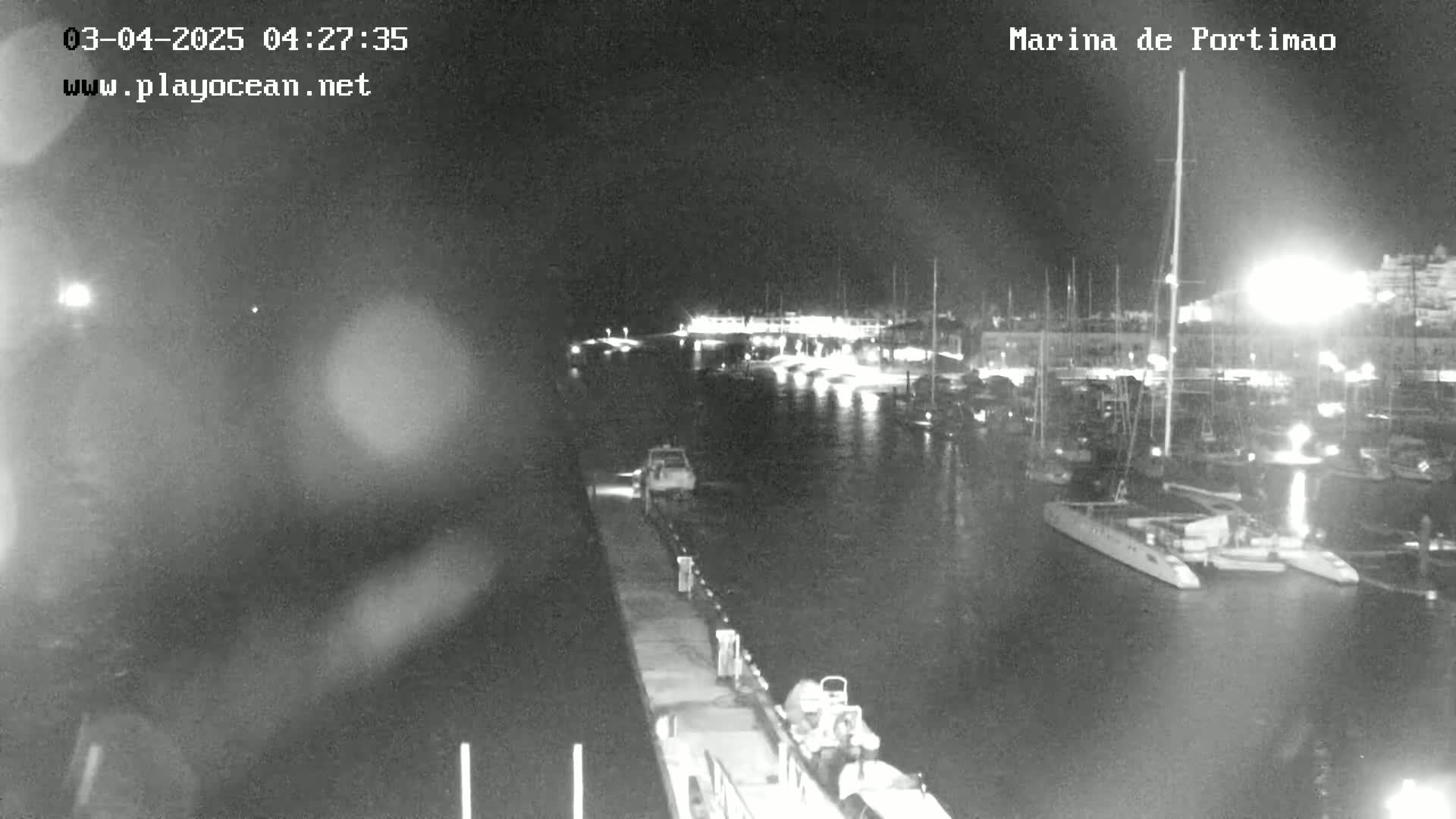 A nighttime, low-light view of a marina filled with boats and yachts, under calm conditions.