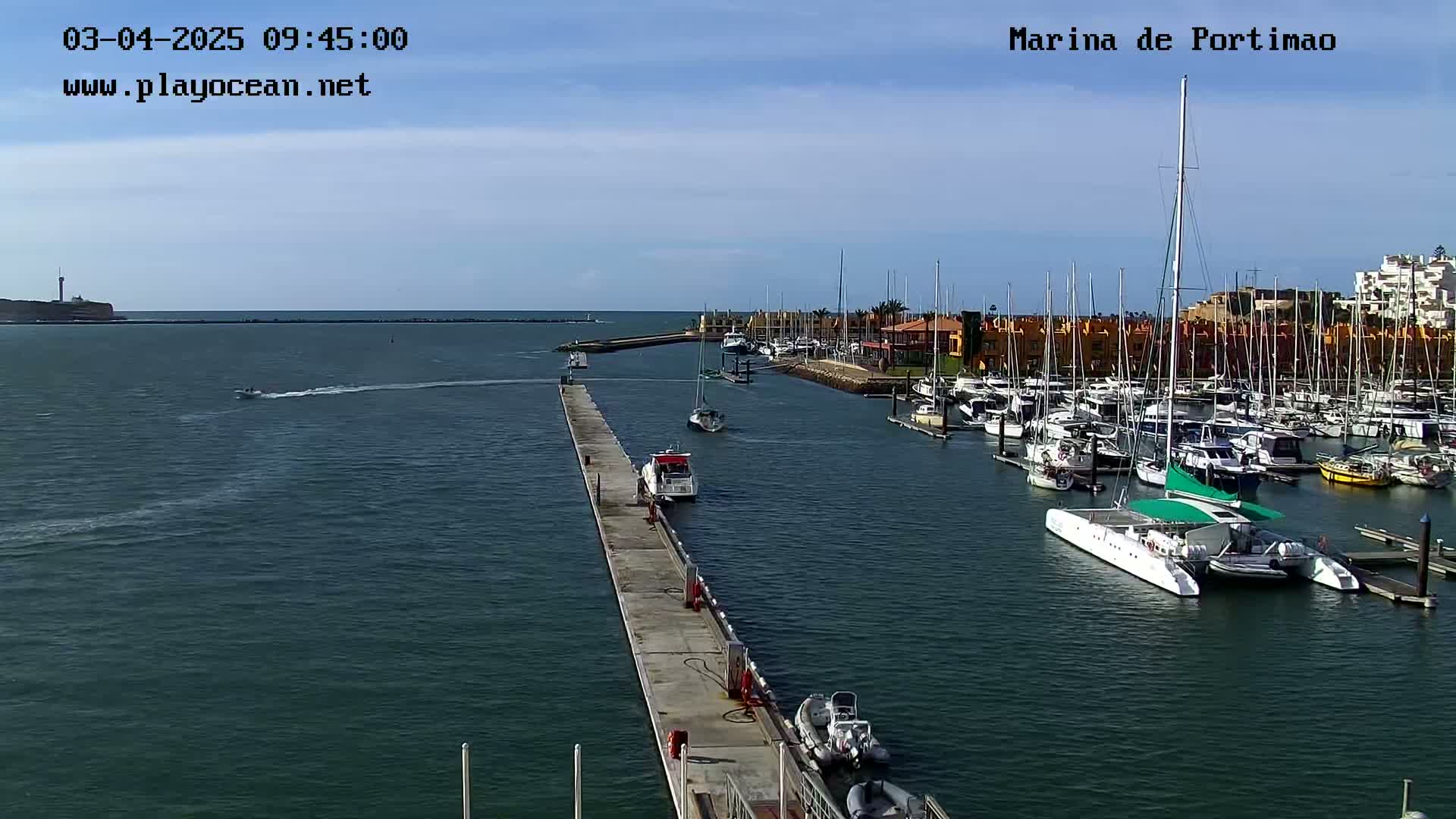 A marina filled with numerous sailboats and motorboats under a clear, sunny sky.