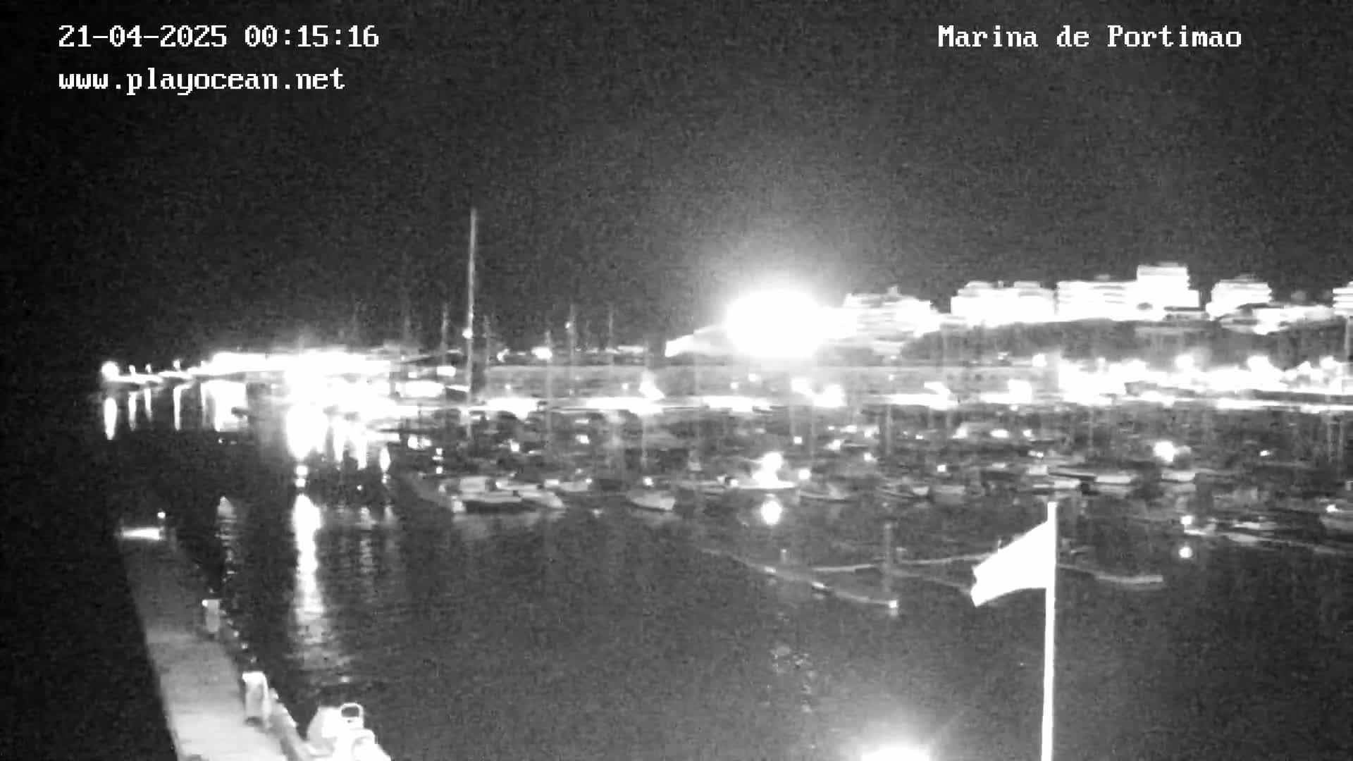 A nighttime, low-light view of a marina filled with boats, with buildings and lights visible in the background.
