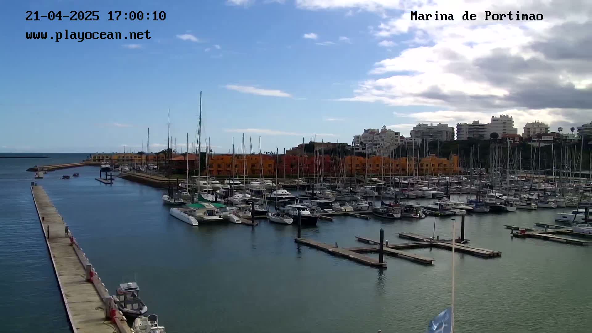 A marina filled with numerous sailboats and motorboats under a partly cloudy sky.