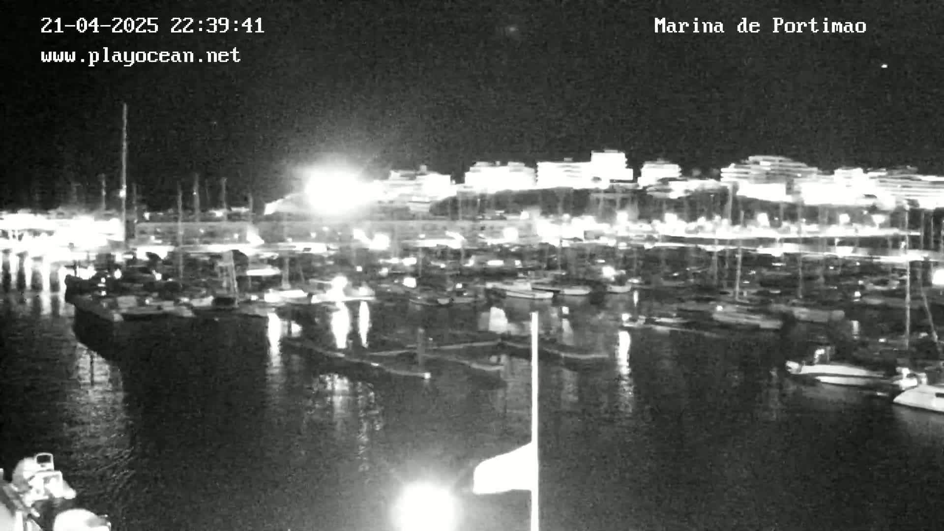 A nighttime, low-light view of a marina filled with boats, with buildings illuminated in the background.