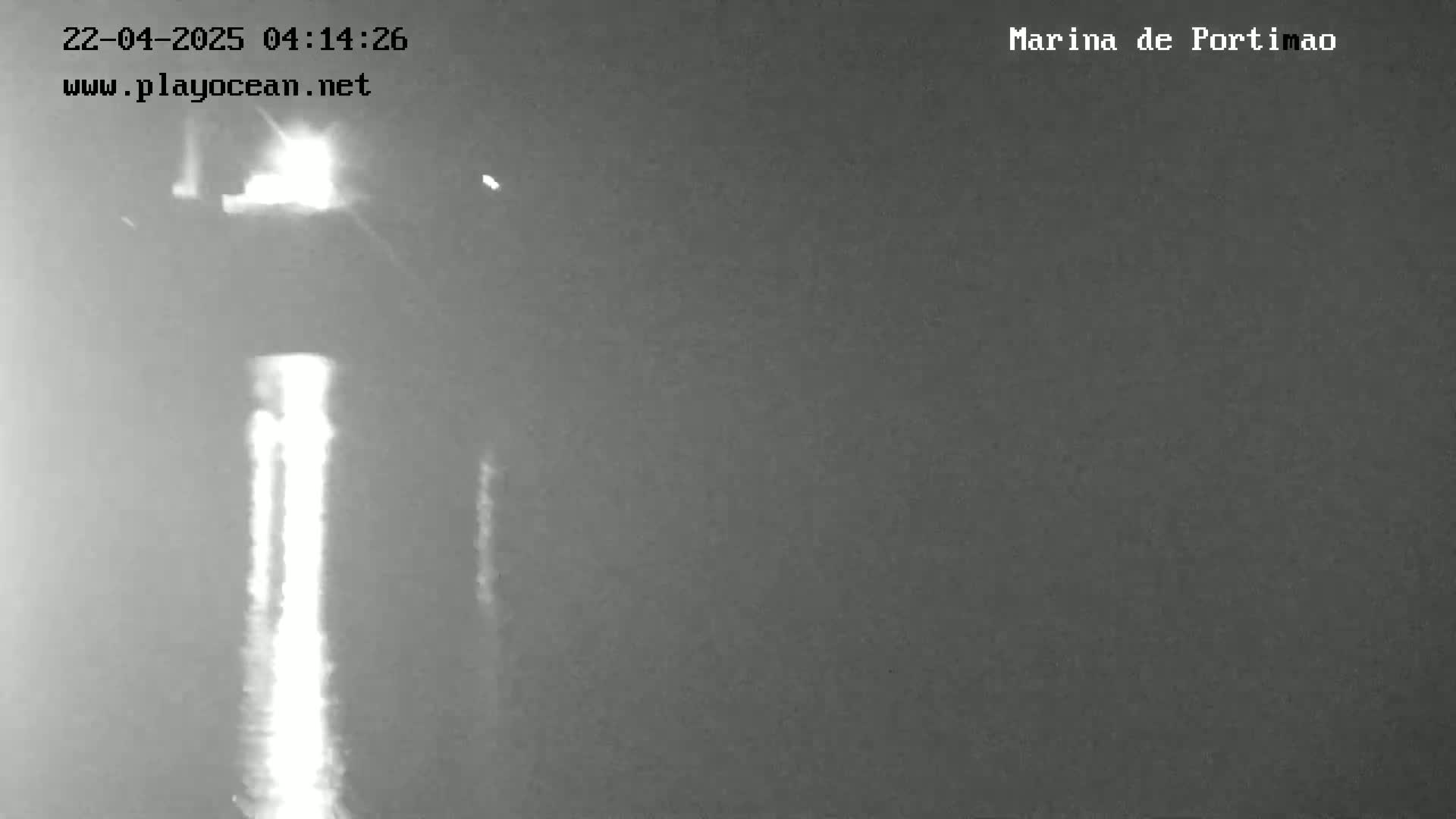 A nighttime, low-light image shows a bright vertical line of light reflecting on dark water.
