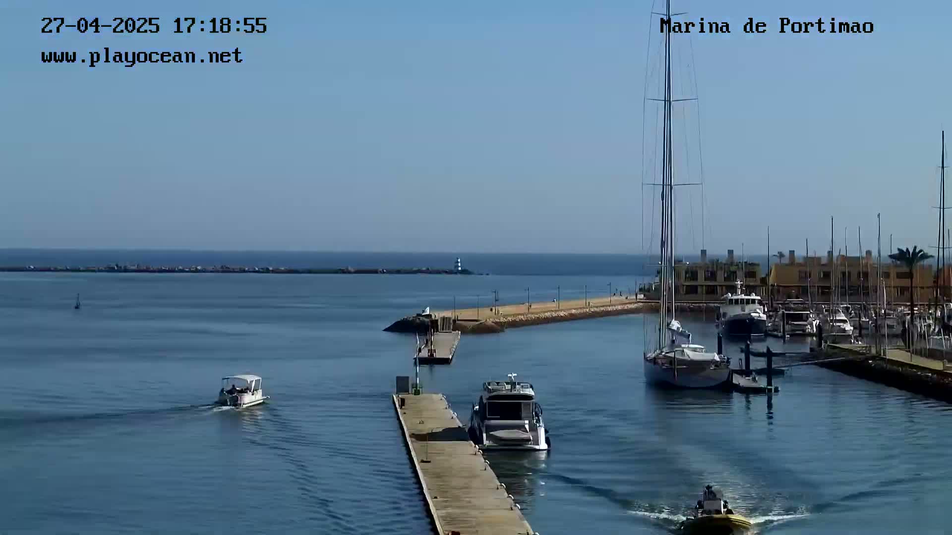 A marina with several boats, including a large sailboat, on a calm, sunny day.