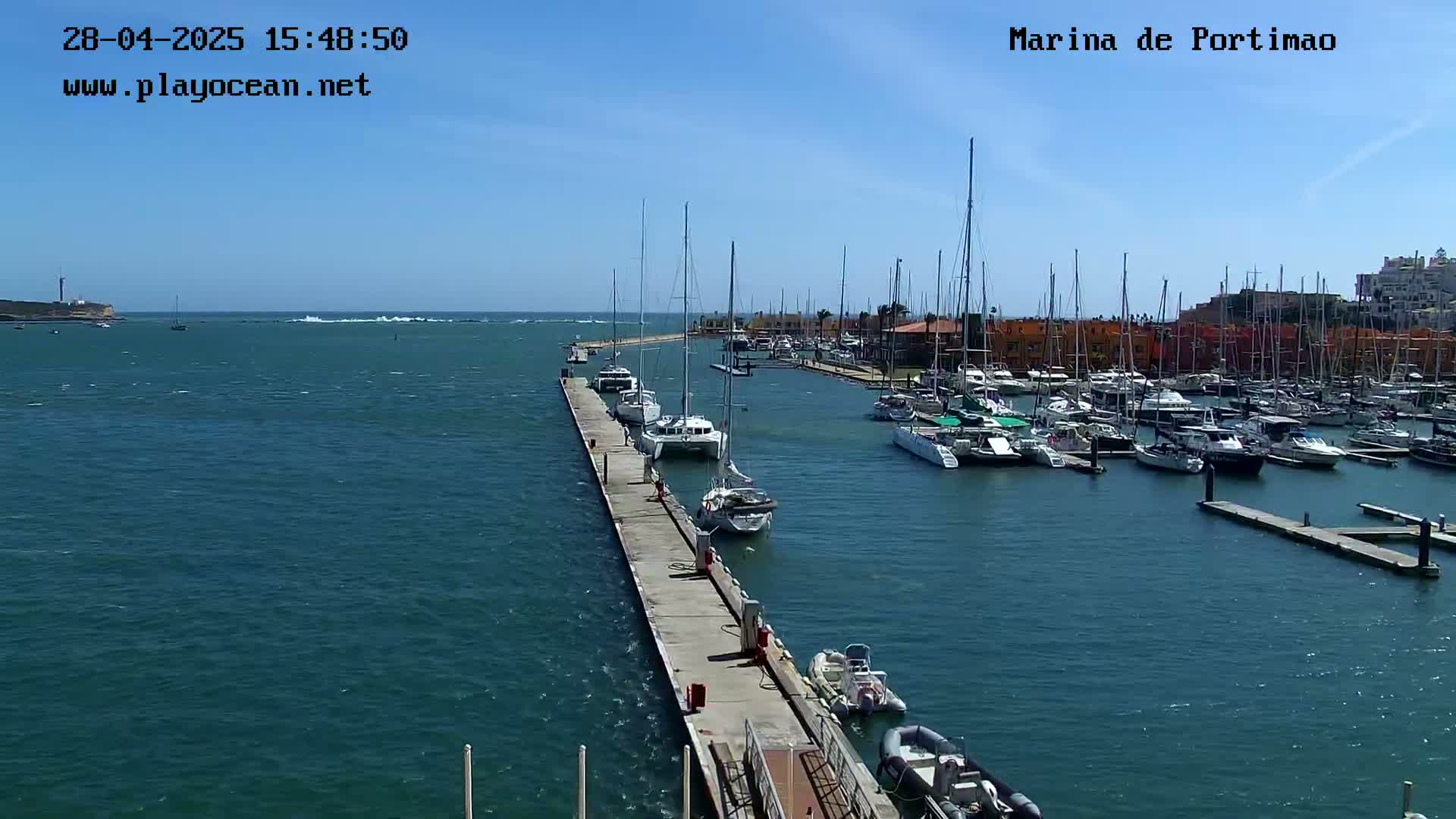 A marina filled with sailboats and motorboats on a sunny day, with a long pier extending into the water.