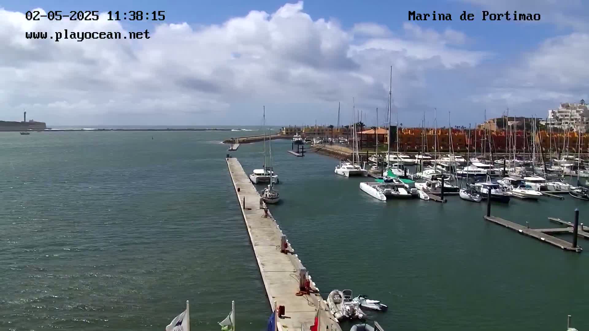 A marina filled with sailboats and motorboats is shown on a partly cloudy day.