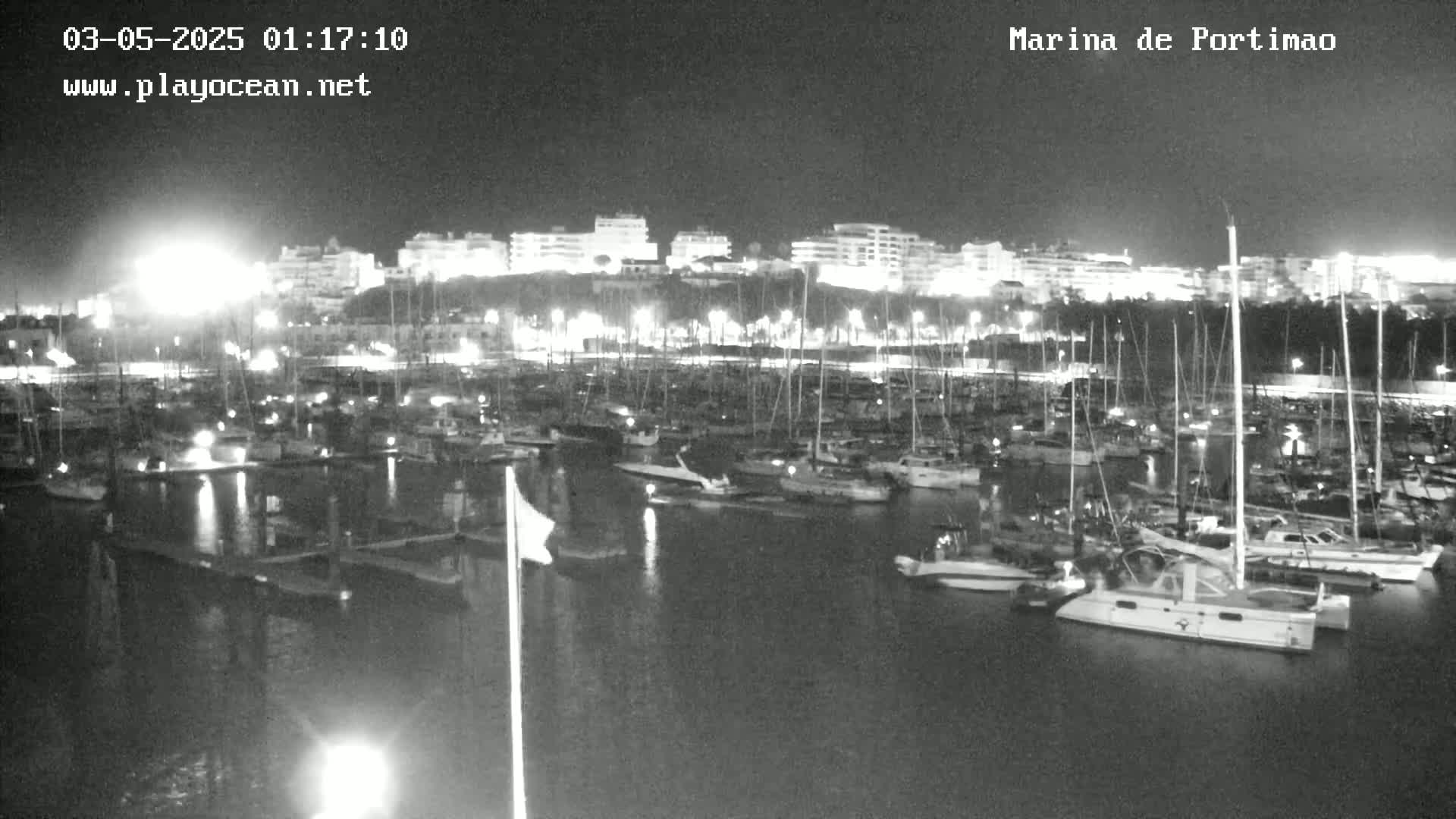 A nighttime, low-light view of a marina filled with numerous boats docked alongside a shoreline with illuminated buildings.