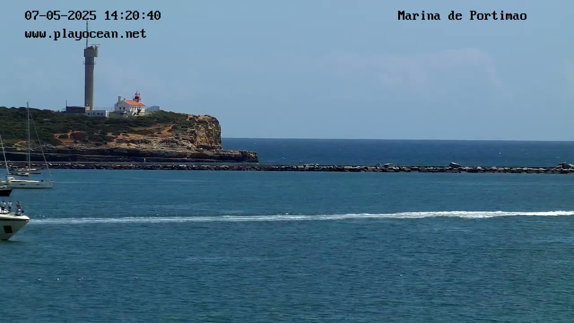 A body of water with several boats, a rocky cliff with a lighthouse, and a clear sky.