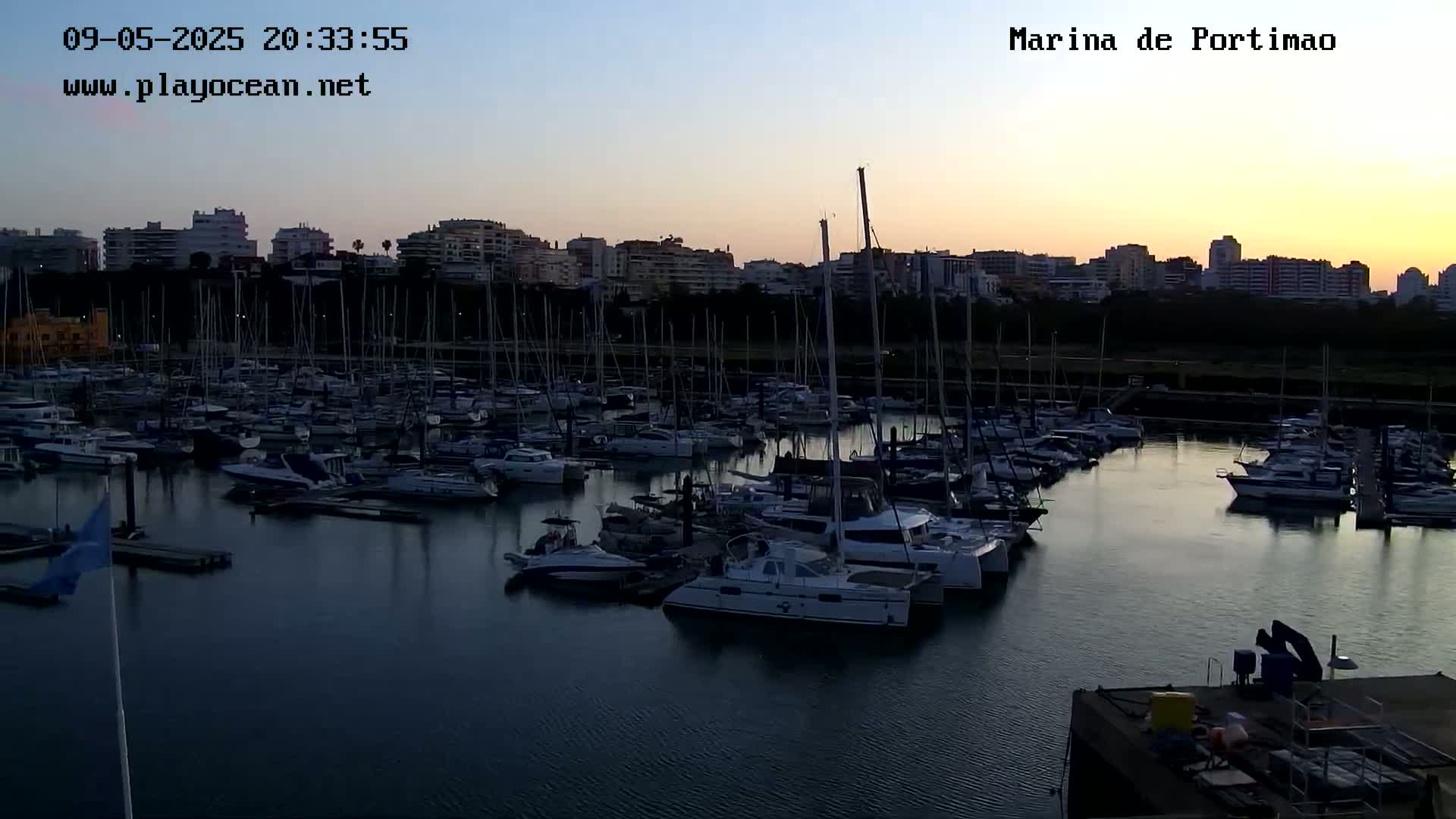 Many boats are moored in a marina at dusk, under a clear, twilight sky.