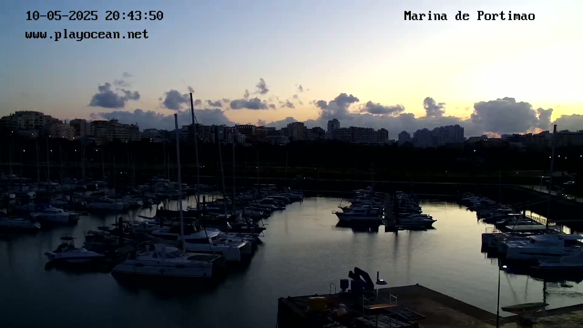 A marina filled with boats at twilight under a partly cloudy sky.