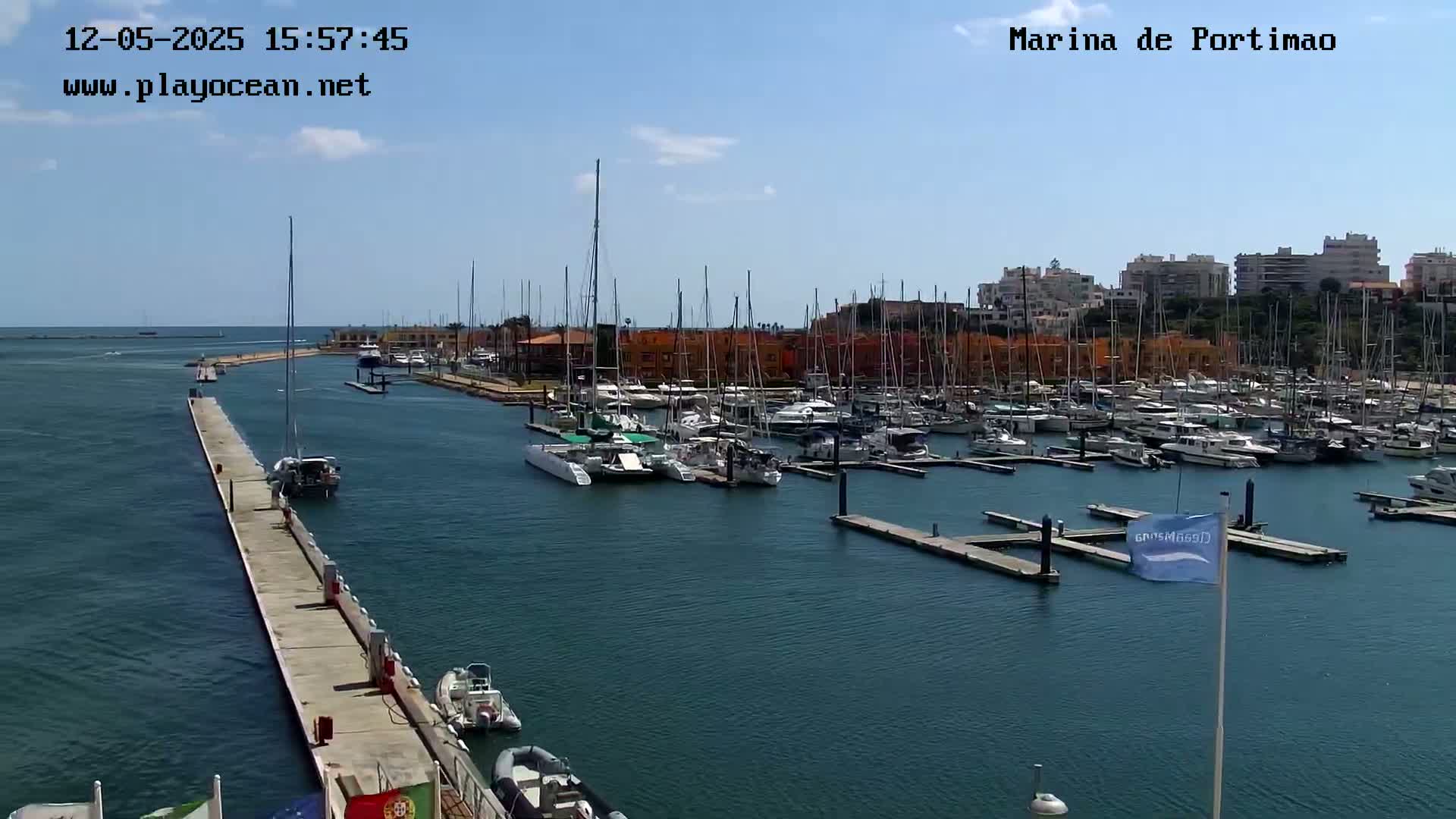 A marina filled with numerous sailboats and motorboats on a sunny day, with a long pier extending into the calm water.