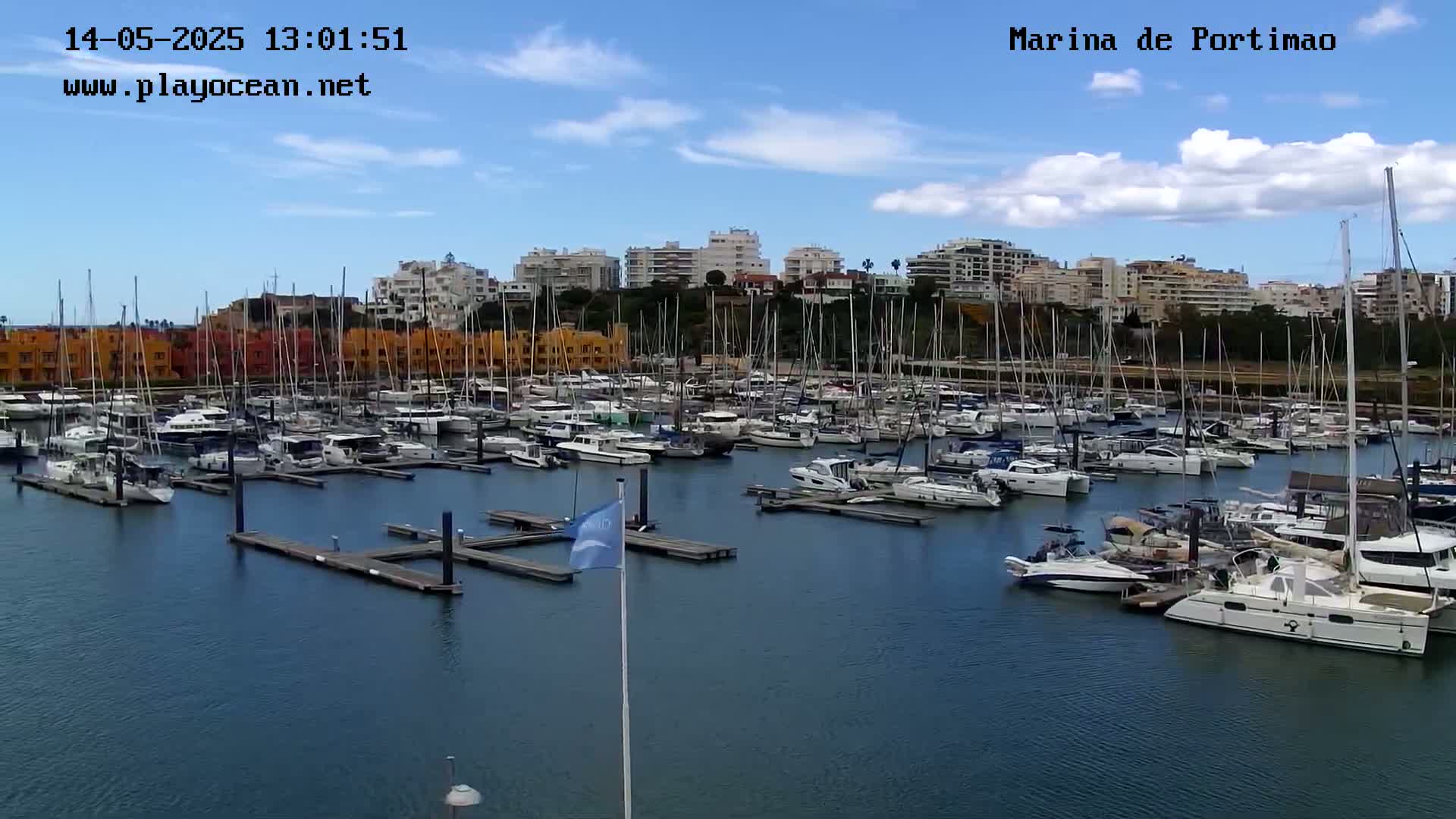 A marina filled with numerous sailboats and motorboats is seen on a partly cloudy day.
