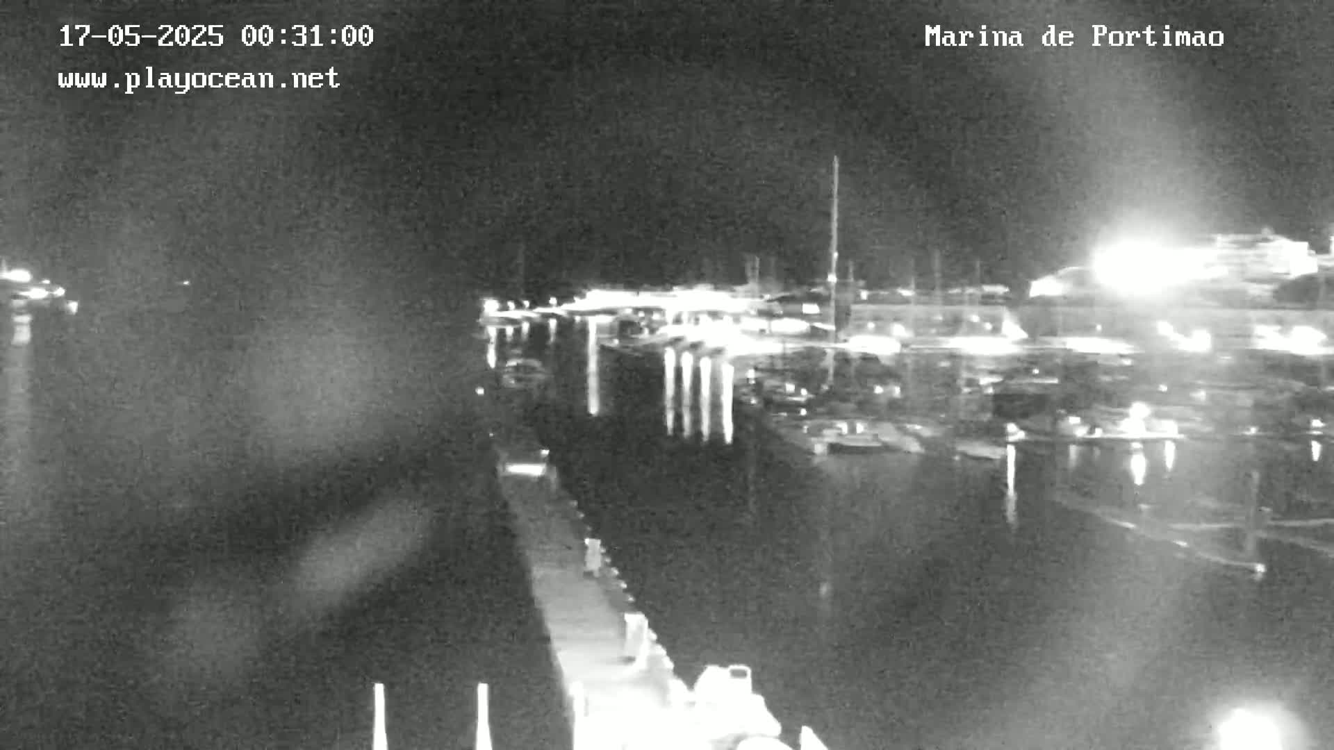 A nighttime, low-light view of a marina filled with boats docked alongside a pier.