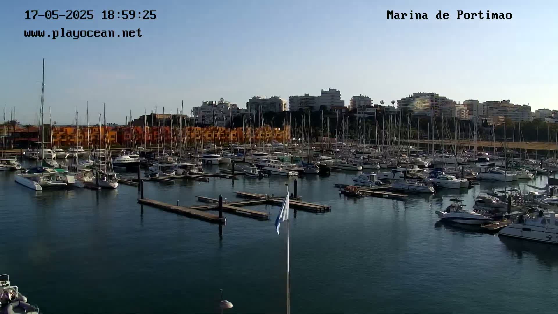 A marina filled with numerous sailboats and motorboats is situated under a clear sky.