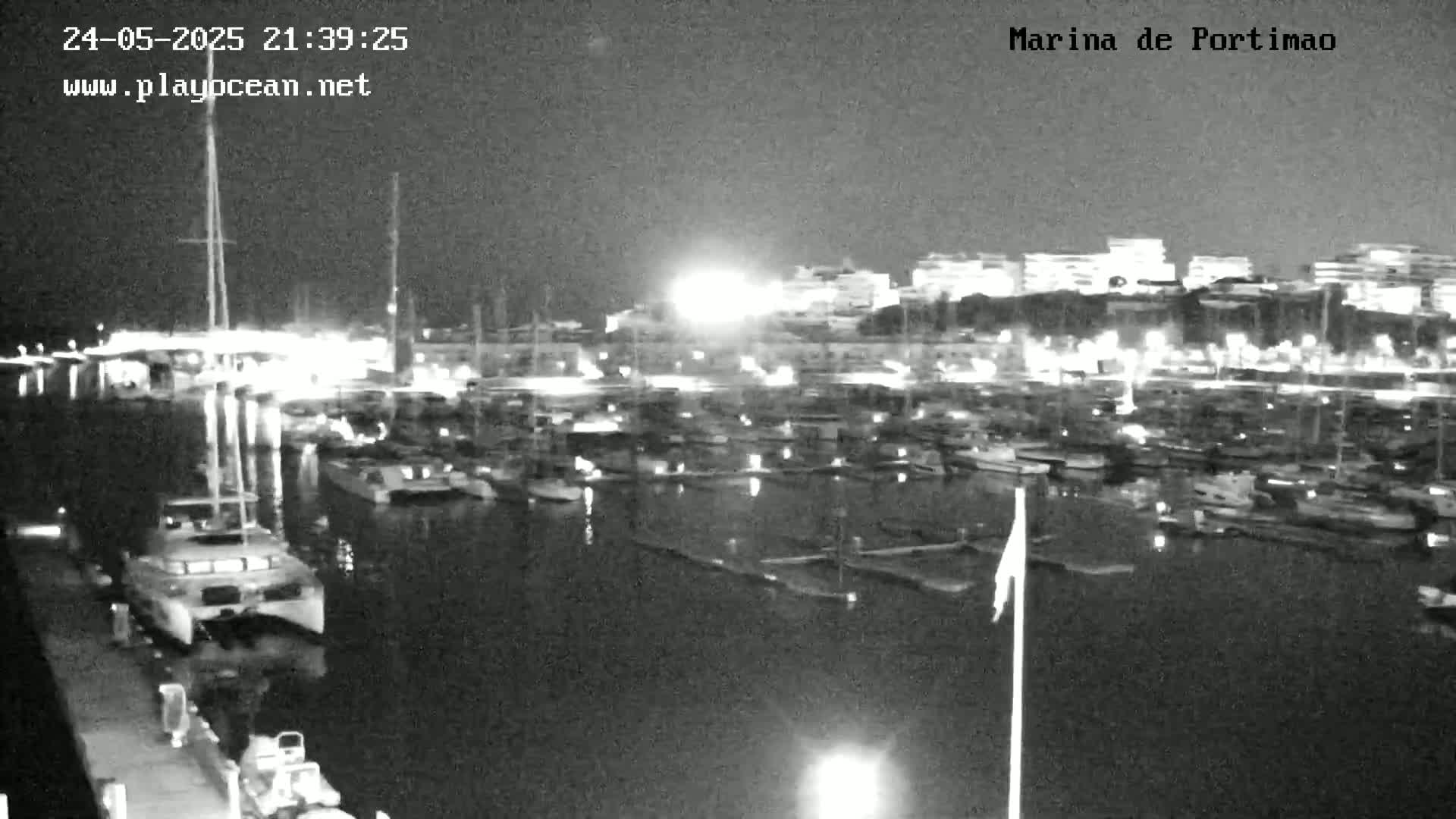 A nighttime, low-light view of a marina filled with numerous boats and yachts, with city lights visible in the background.