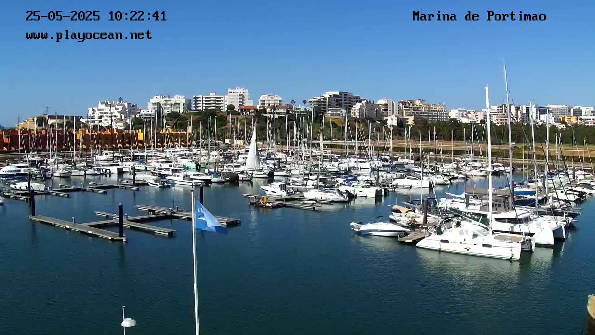 A marina filled with numerous sailboats and motorboats is seen on a sunny day.
