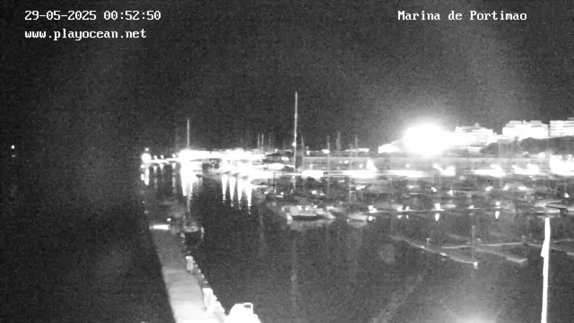 A nighttime, low-light view of a marina filled with boats, with lights visible on the surrounding buildings.
