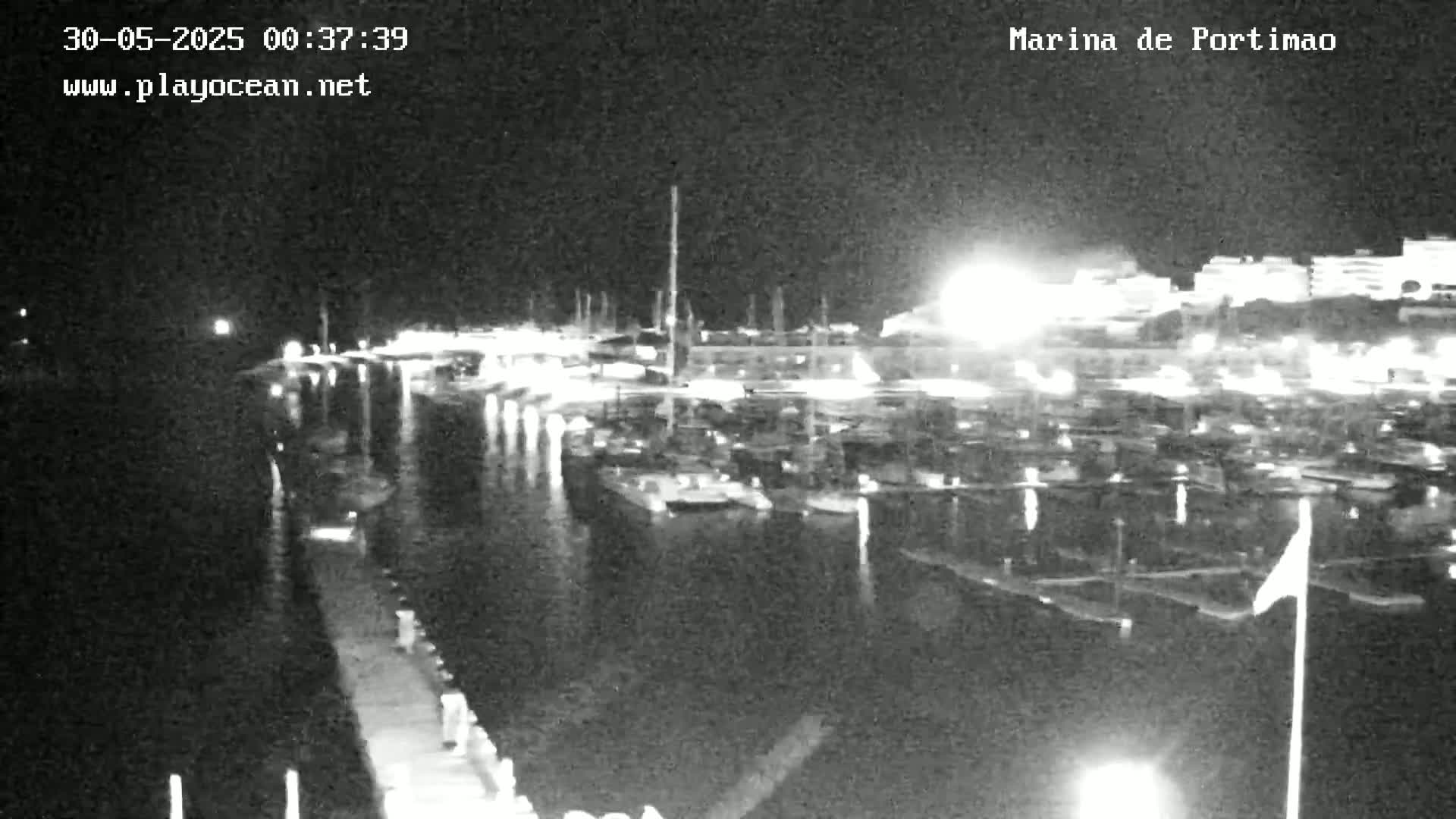 A nighttime, black and white view of a marina filled with boats docked along a pier.
