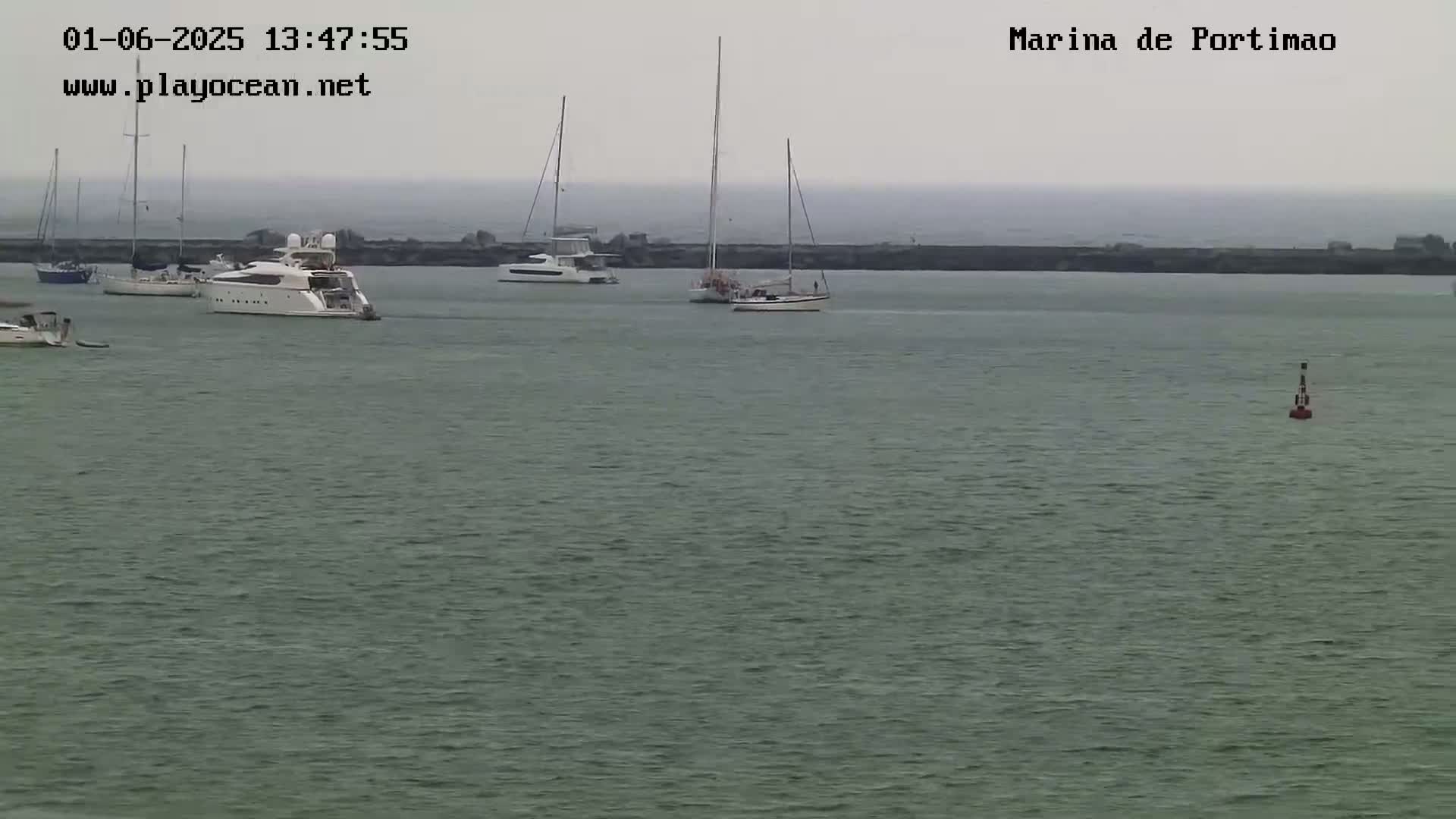 Several boats and yachts are moored in a calm, gray-toned harbor under an overcast sky.