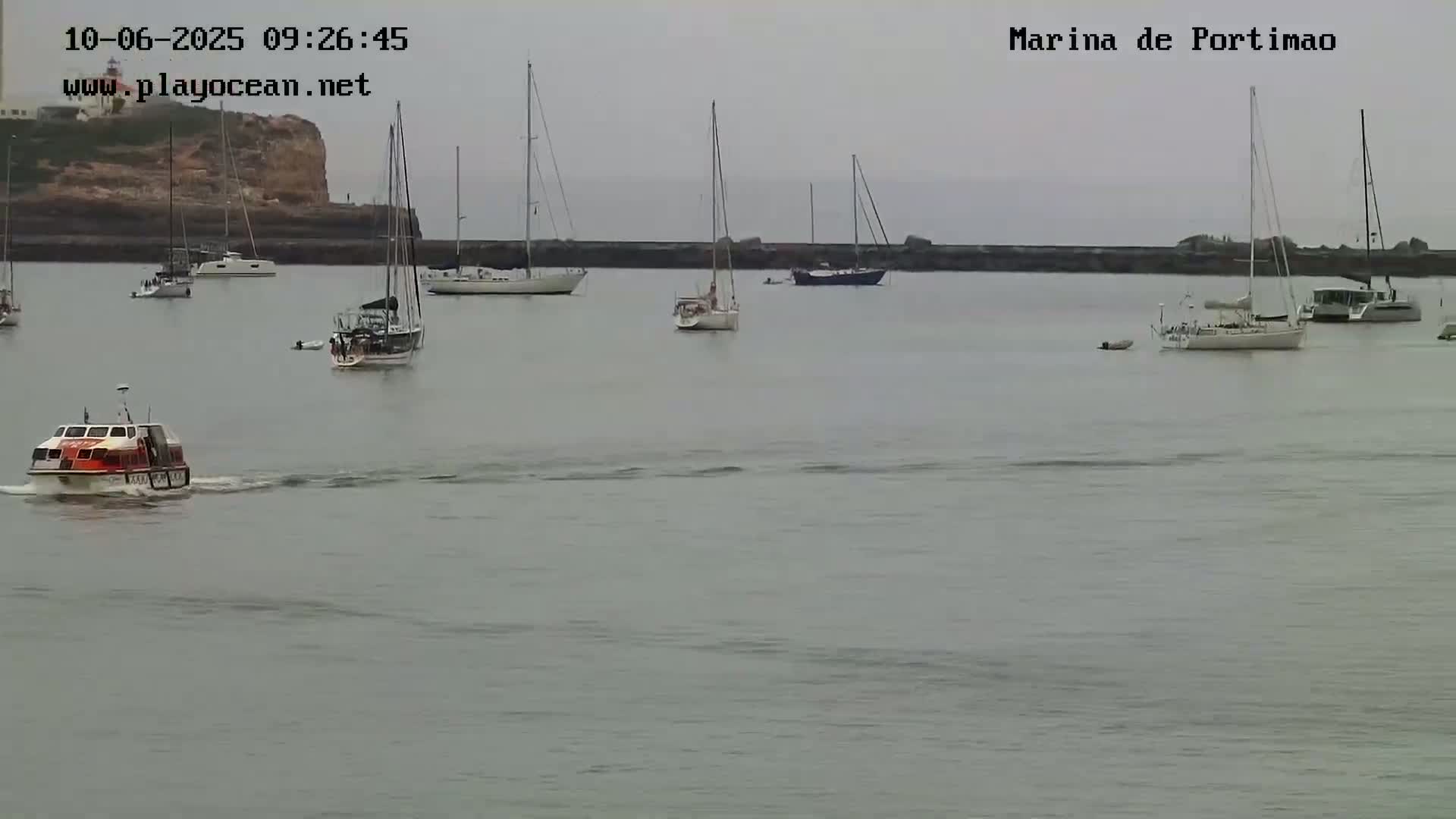 A calm, overcast day shows a harbor filled with sailboats and a small rescue boat.