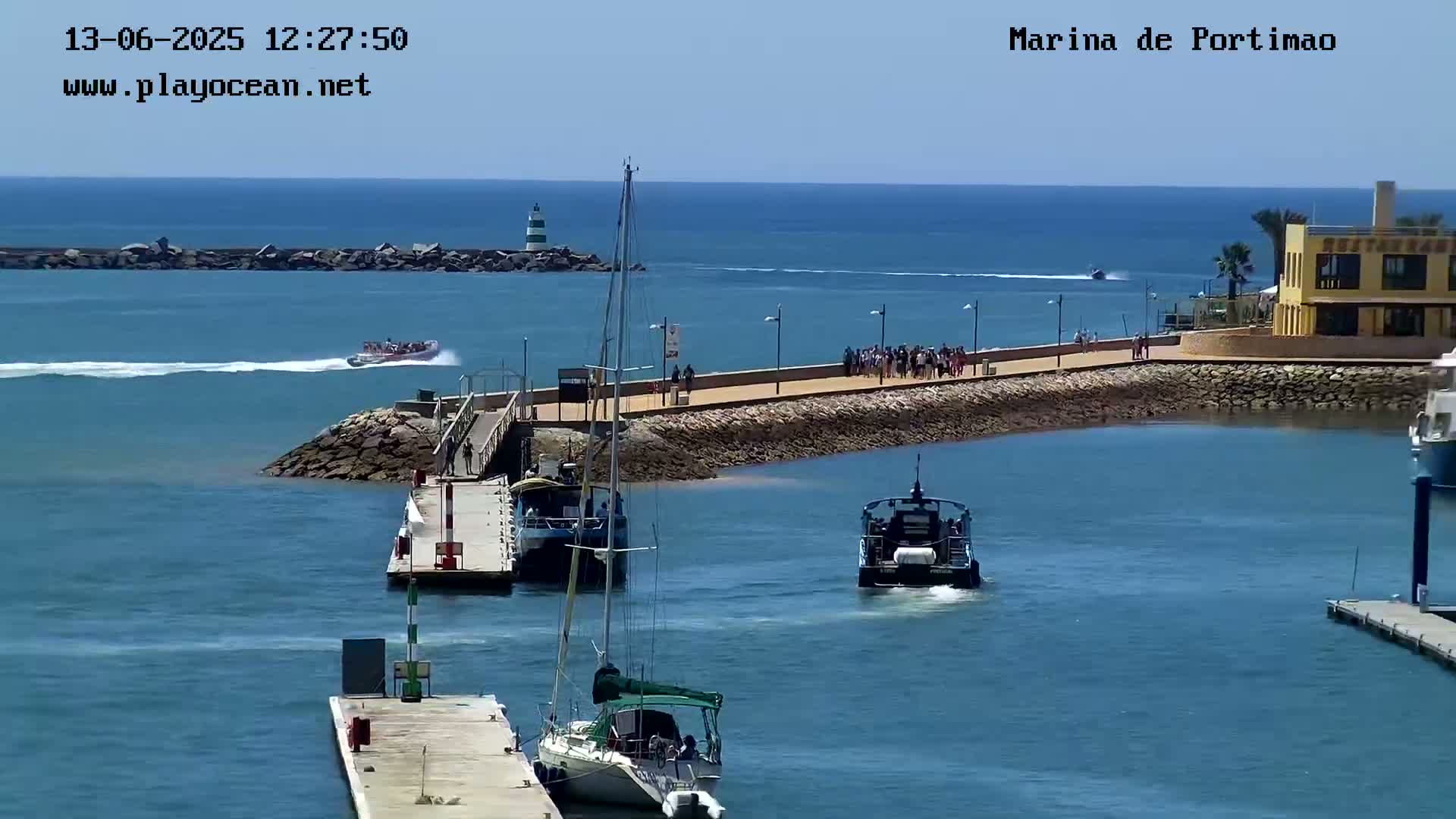 A marina with several boats, including a sailboat and a small passenger ferry, on a sunny day with calm waters.