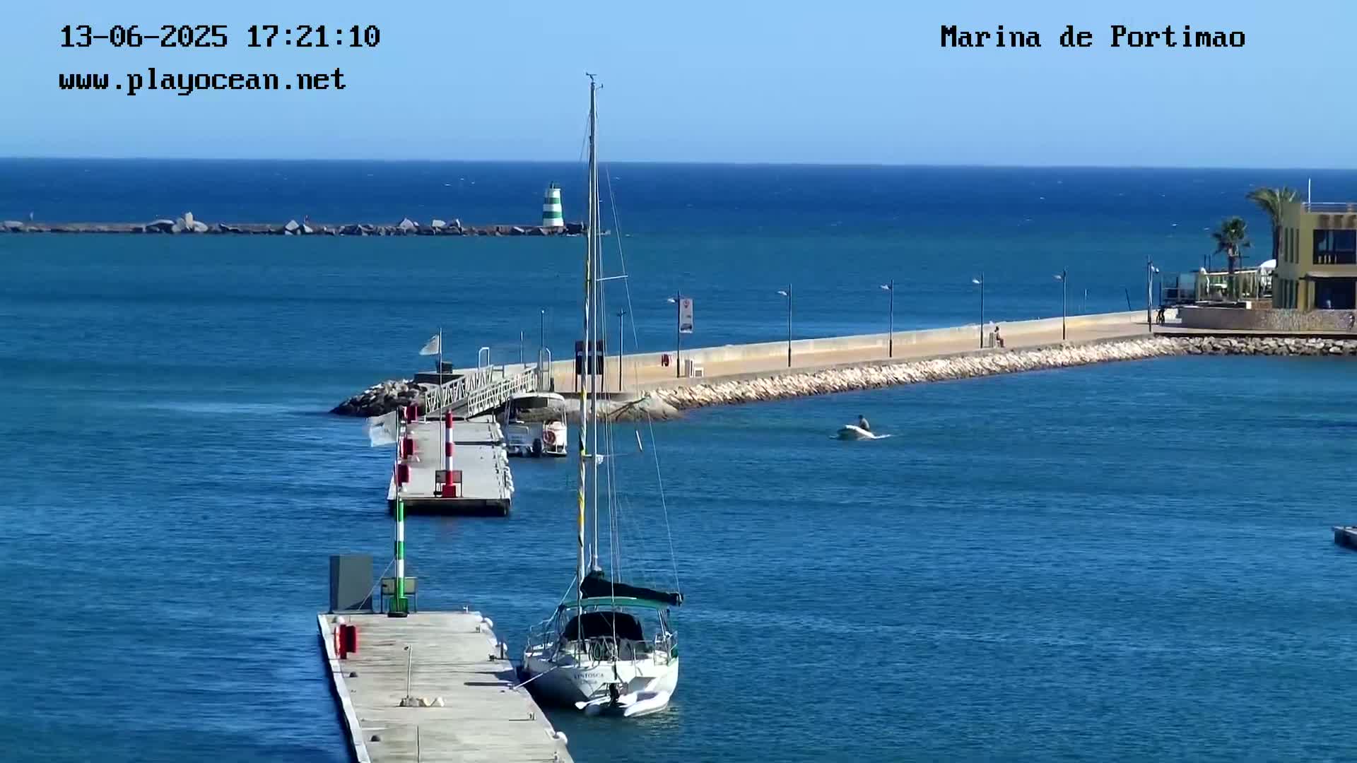 A sailboat is docked at a marina on a sunny day with calm, blue water.