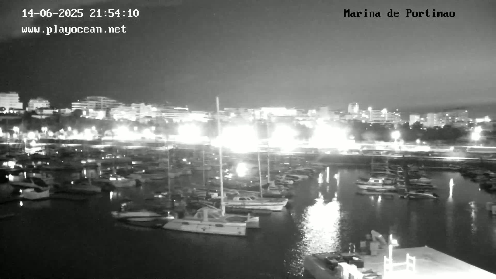 A marina filled with numerous boats and yachts is situated near a city skyline under a partly cloudy sky.