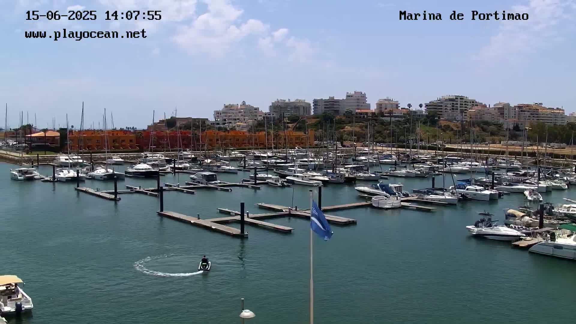 A marina filled with numerous boats and yachts under a partly sunny sky, with a jet ski visible in the water.