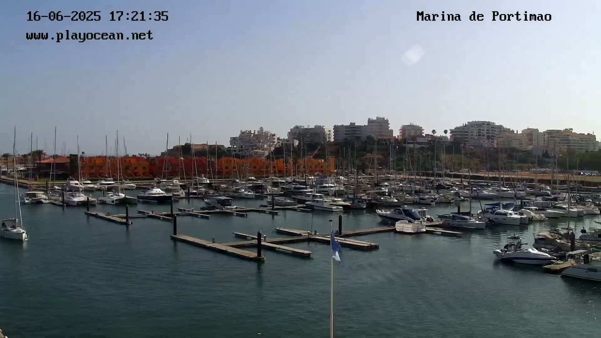A marina filled with numerous sailboats and motorboats is seen under a clear sky.