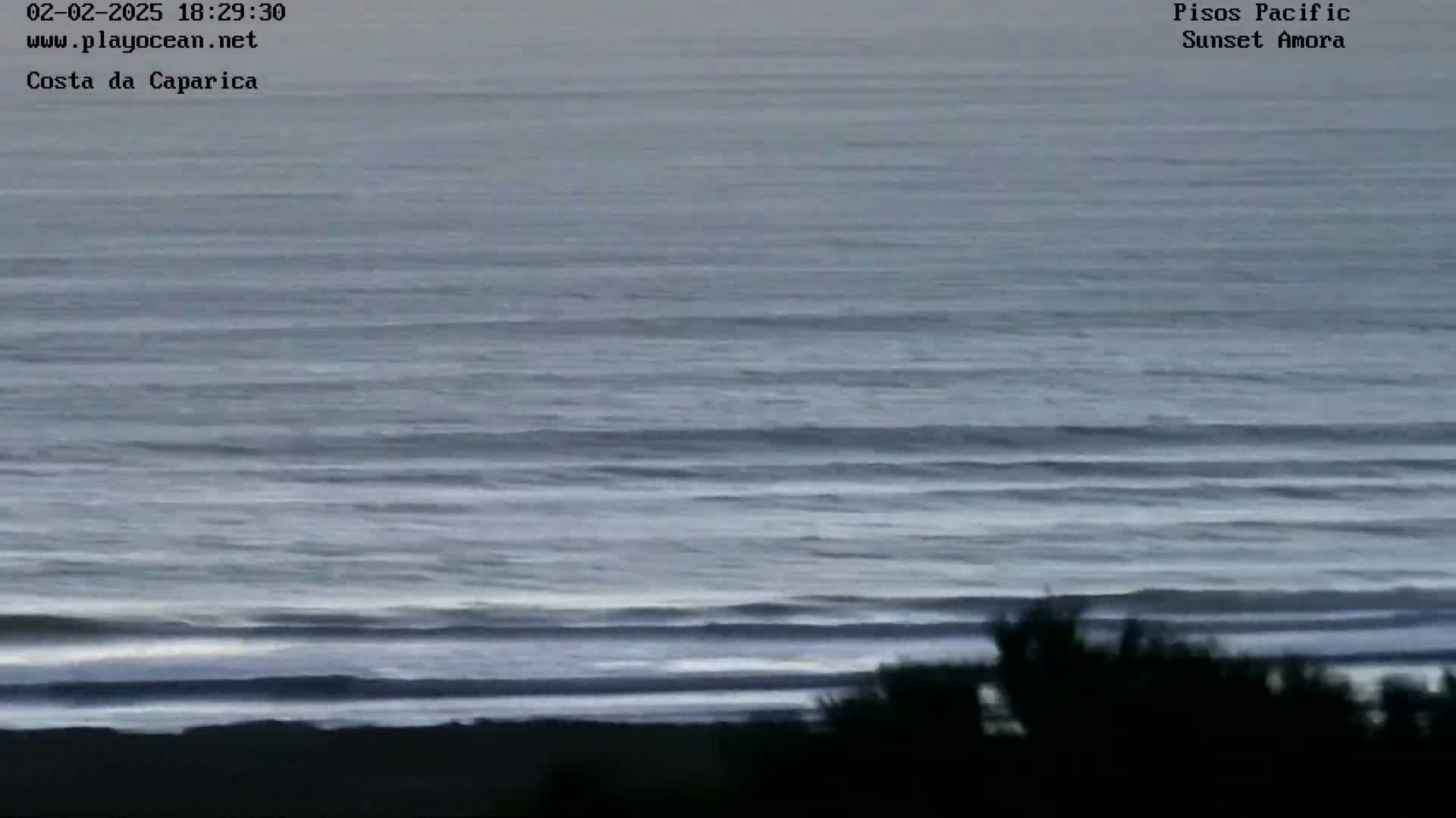 A dark, overcast sky hangs over a calm, grey ocean meeting a dark shoreline with some silhouetted vegetation.