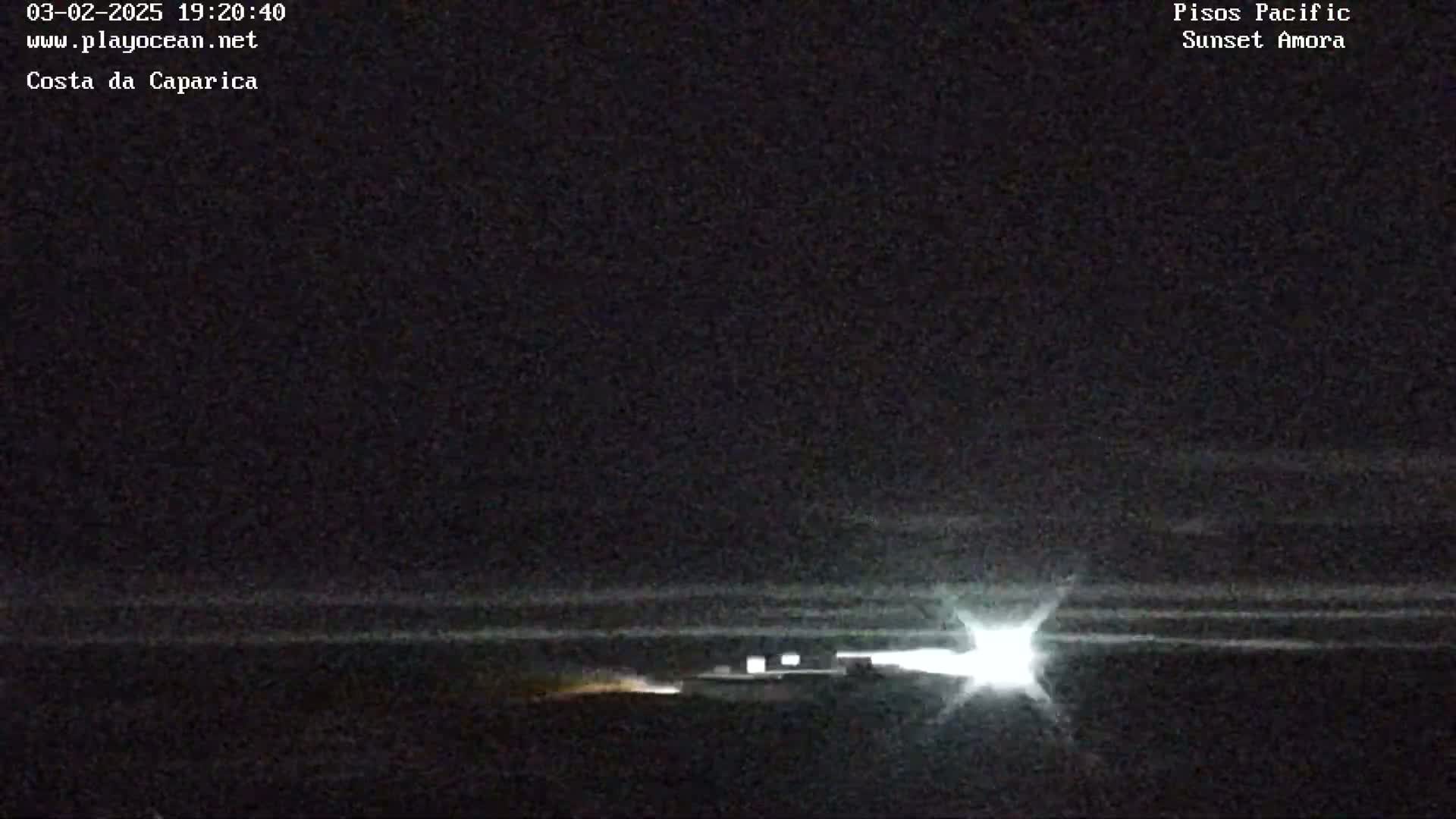 A nighttime, low-light image shows a bright light source in the distance, possibly headlights, with a dark, flat expanse in the foreground.