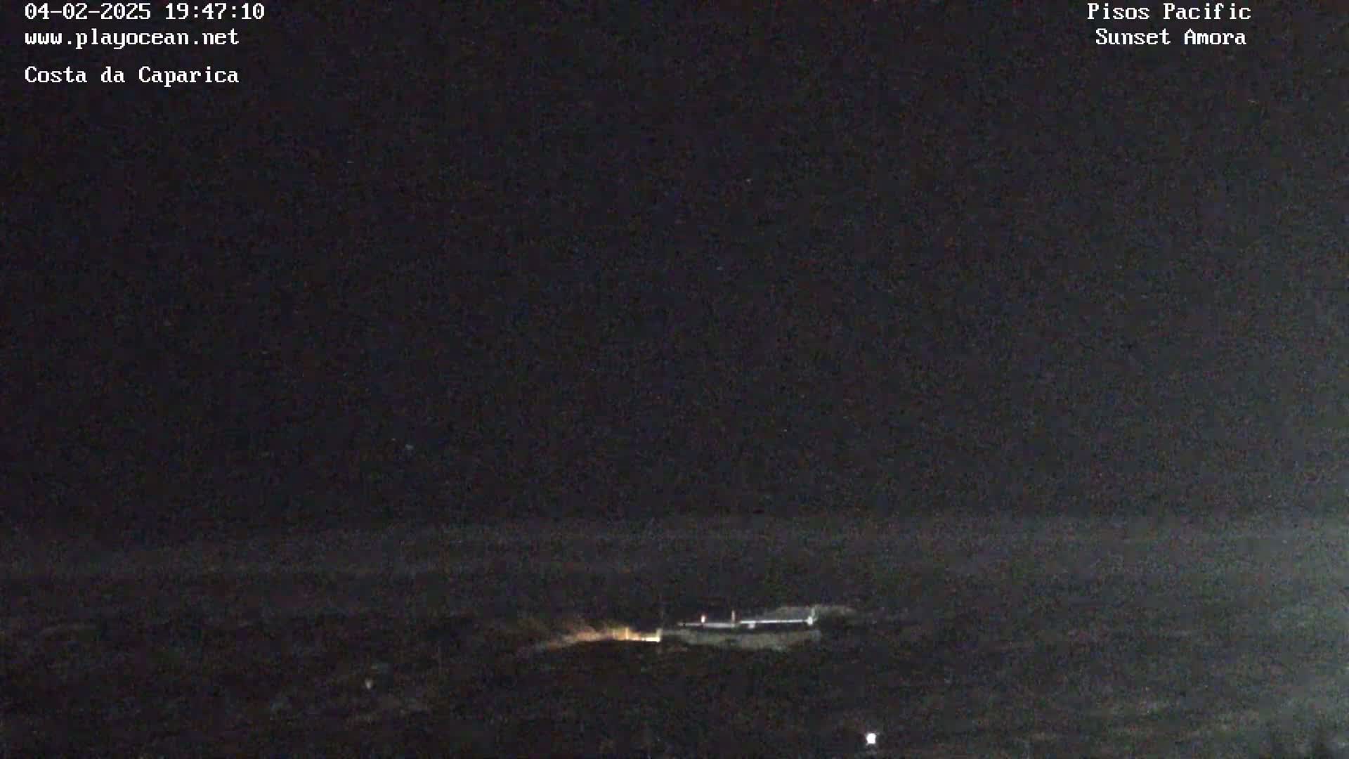 A nighttime, dark view of a low-lying structure near the ocean under a clear, dark sky.