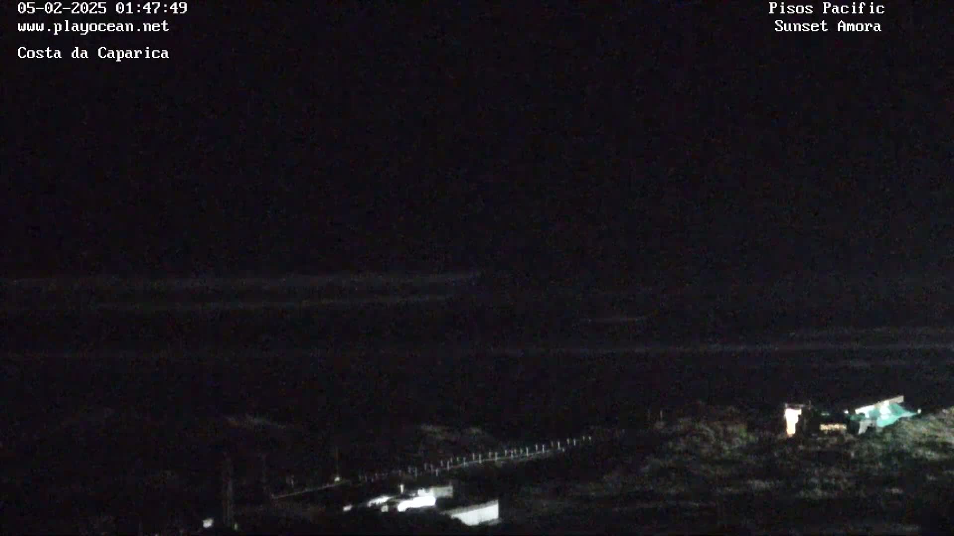 A nighttime, low-light view of a dark ocean and a dimly lit shoreline.