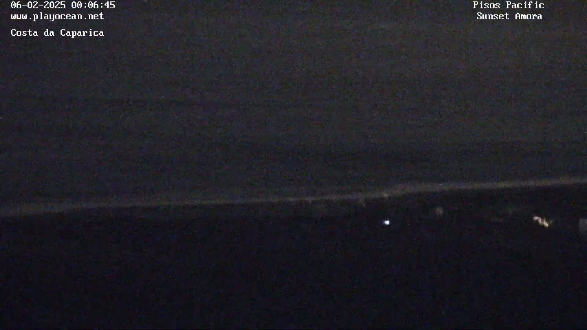 A dark, nighttime view of a coastline shows a dark ocean and a dark landmass with a few small lights visible.
