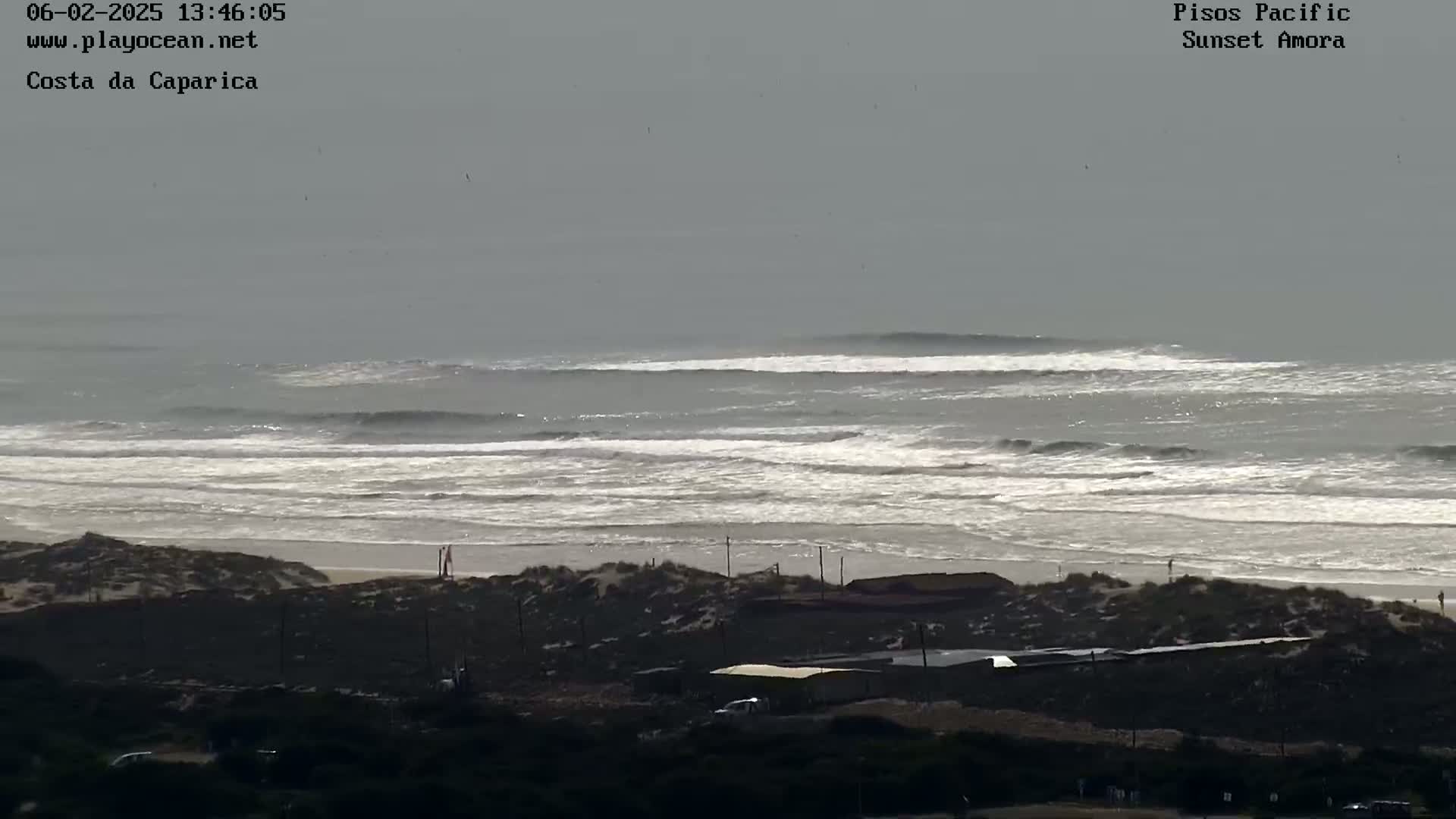 A long, wide expanse of ocean with moderately sized waves rolling onto a sandy beach under an overcast sky.