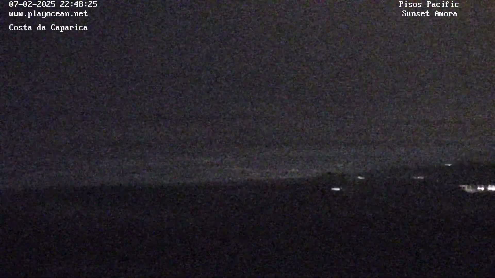 A nighttime long shot shows a dark ocean horizon with a few distant lights visible along the shoreline under a mostly clear, dark sky.
