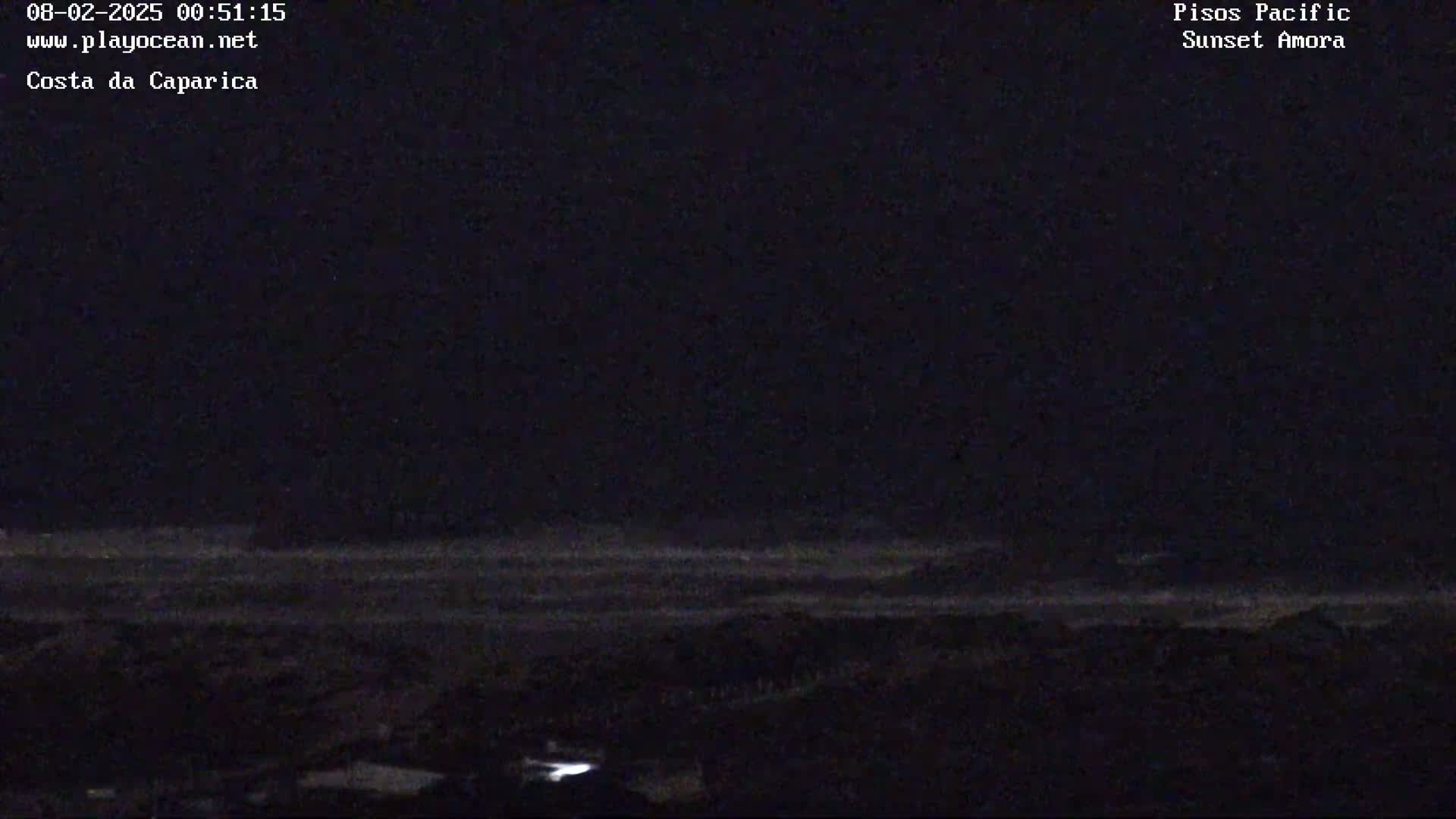 A dark nighttime coastal scene shows a faint, barely visible ocean and land under a clear, dark sky.