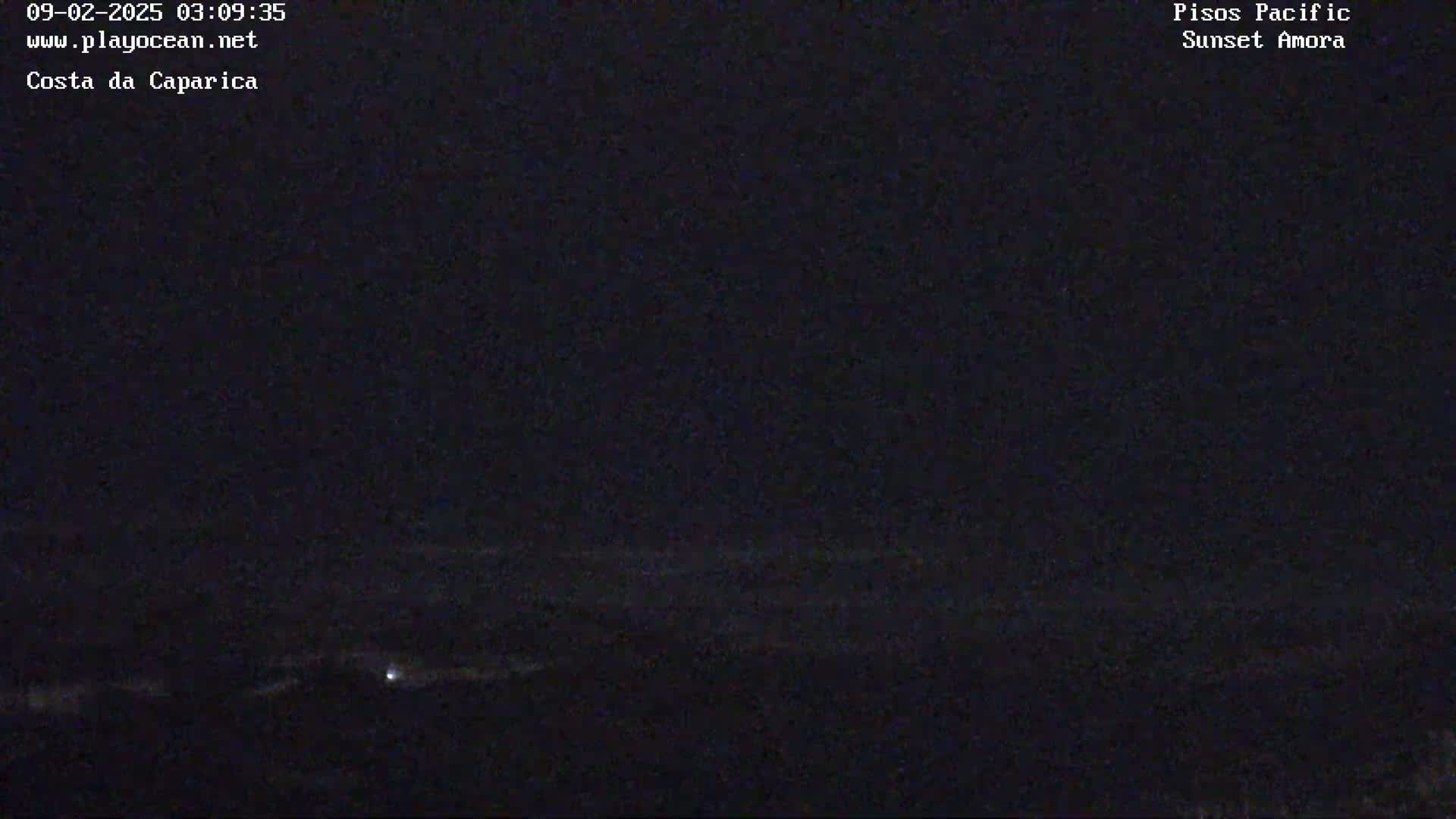 A dark, nighttime view of a coastline with a faint light visible in the distance.