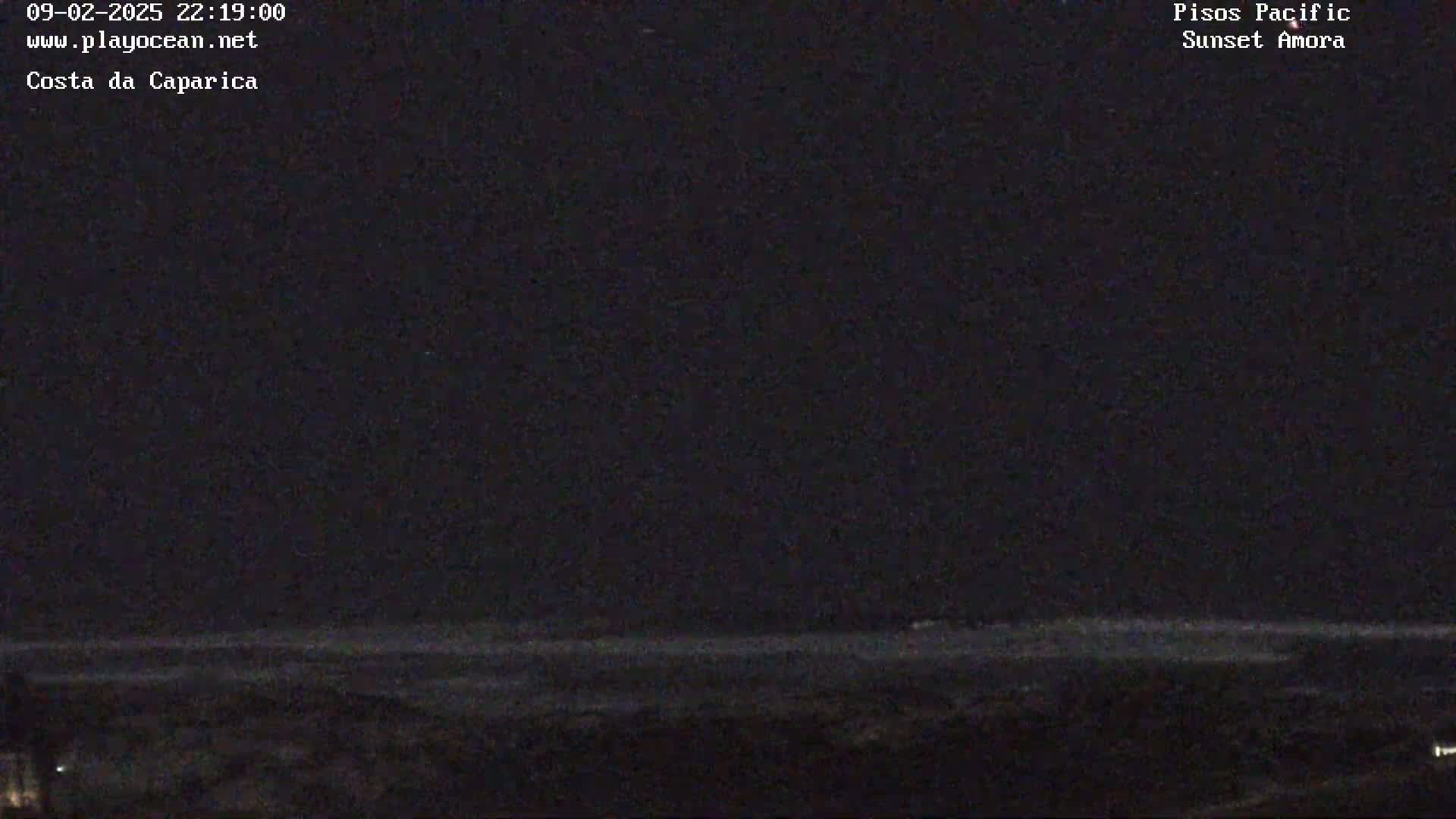 A dark nighttime coastal scene shows a barely visible ocean horizon under a clear, dark sky.