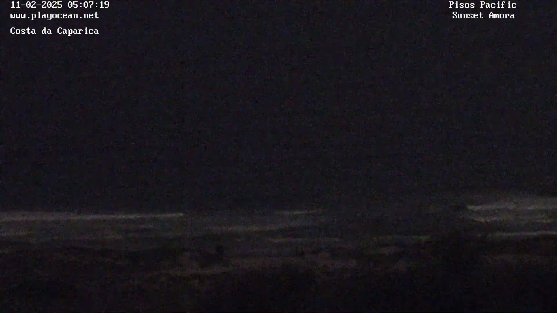 A dark nighttime view of a beach with a mostly calm ocean under a clear, dark sky.